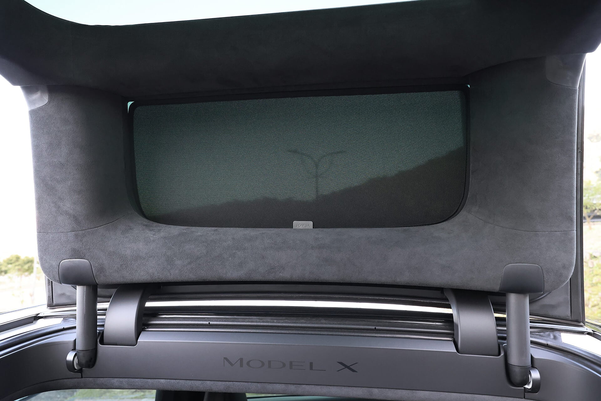 特斯拉 Model X 後車廂特寫,後備箱打開,展示後窗上的 JOWUA Taiwan 分離式遮陽簾 (Model X)、車廂內的 Model X 標籤,以及專為其鷹翼門設計的功能。.