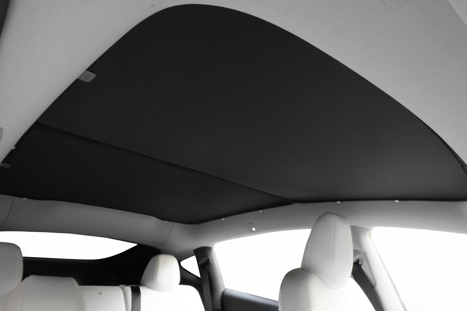 Tesla Model Y 車內車頂視圖,配有封閉式 JOWUA 台灣玻璃車頂遮陽簾(Model Y 煥新版 2025+/2021-2024),全景玻璃上採用抗光銀塗層,加上白色頭枕和座椅,非常適合您的升級。.