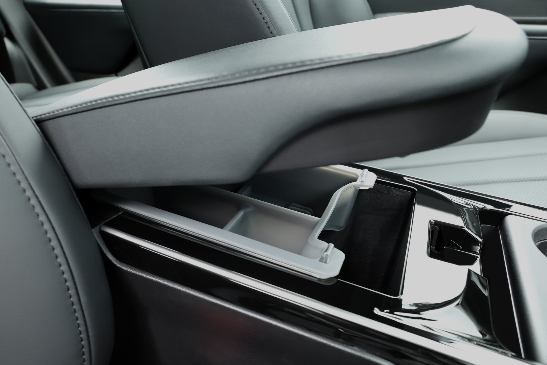 JOWUA 台灣扶手箱收納盒(LUXGEN n⁷ 專用)的特寫,展示了開放式雙層設計收納隔間。抬起的扶手露出了寬敞的扶手箱空間,並配有黑色內部和光澤的飾面。.