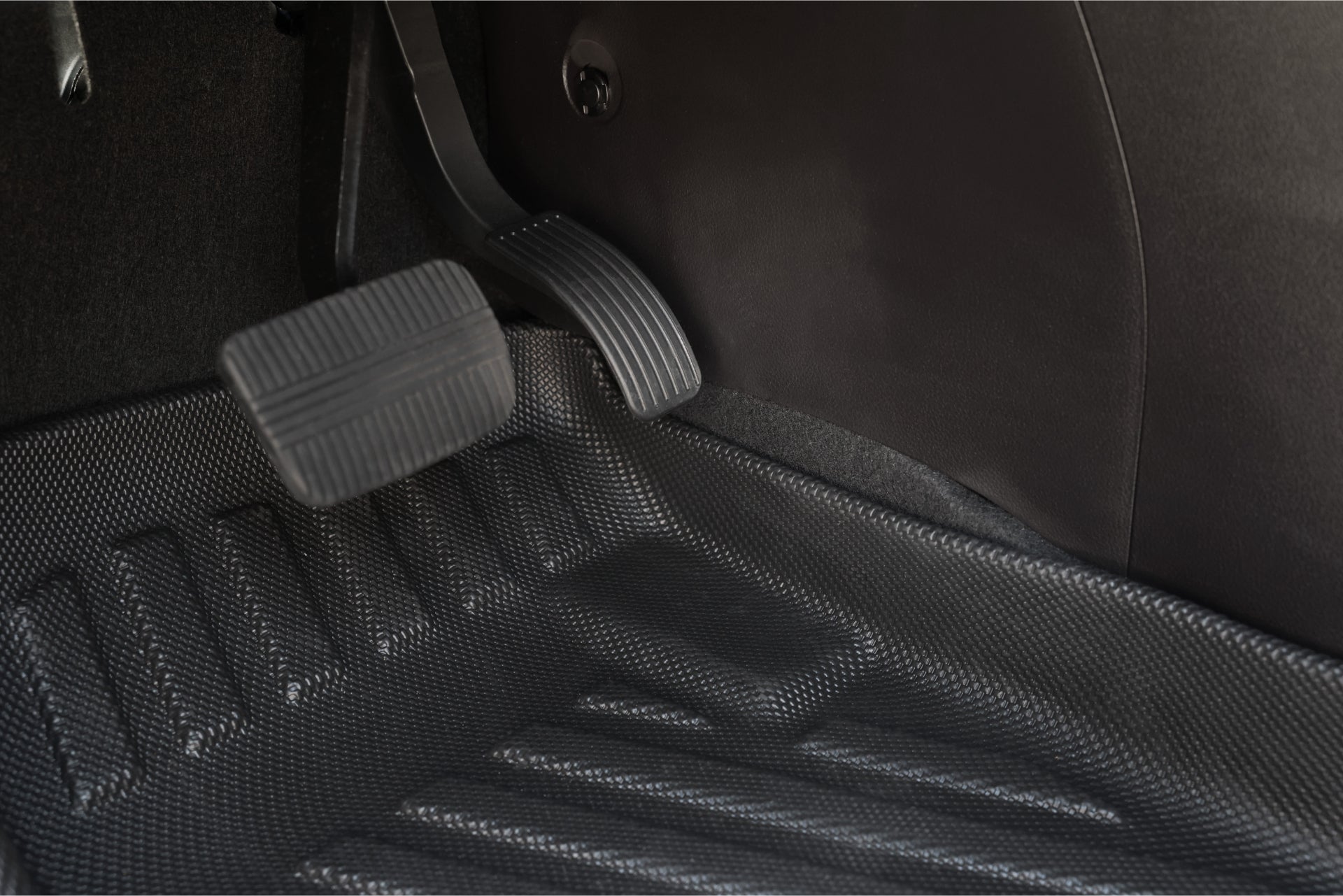 特寫 LUXGEN n⁷ 車內腳踏板空間,採用 JOWUA 台灣立體防水腳墊,煞車和油門踏板位於紋理橡膠墊上方。凹槽的踏板表面增強了安全性,同時該區域的清潔度體現了周到的設計。.