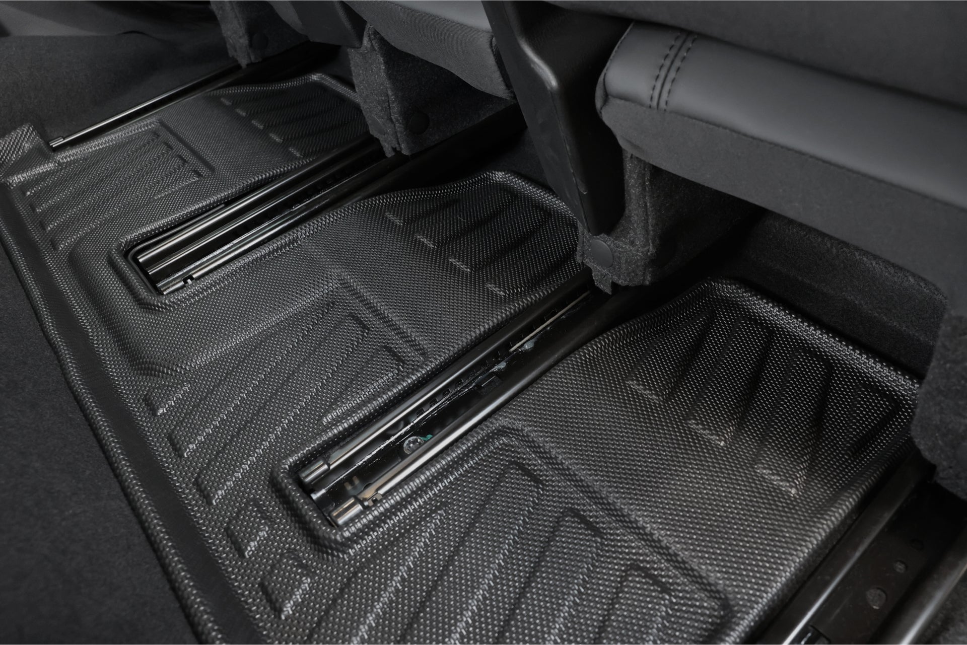 為納智捷LUXGEN n⁷ 7人座量身訂製的JOWUA台灣立體防水腳踏墊特寫。這些黑色橡膠墊具有帶有脊和凹槽的紋理表面,可保護車輛內部免受灰塵和濕氣的侵襲,尤其是後座腳部空間的下方和周圍。.