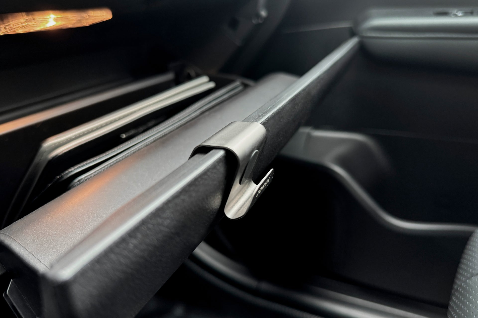 特寫汽車打開的手套箱,可以看到裡面整齊地塞放著文件,內部光滑、深色,LUXGEN n⁷ 手套箱掛鎛鉤門上配有 JOWUA Taiwan 304 不銹鋼閂鎖。陽光輕輕地照亮了儀表板的一部分。.
