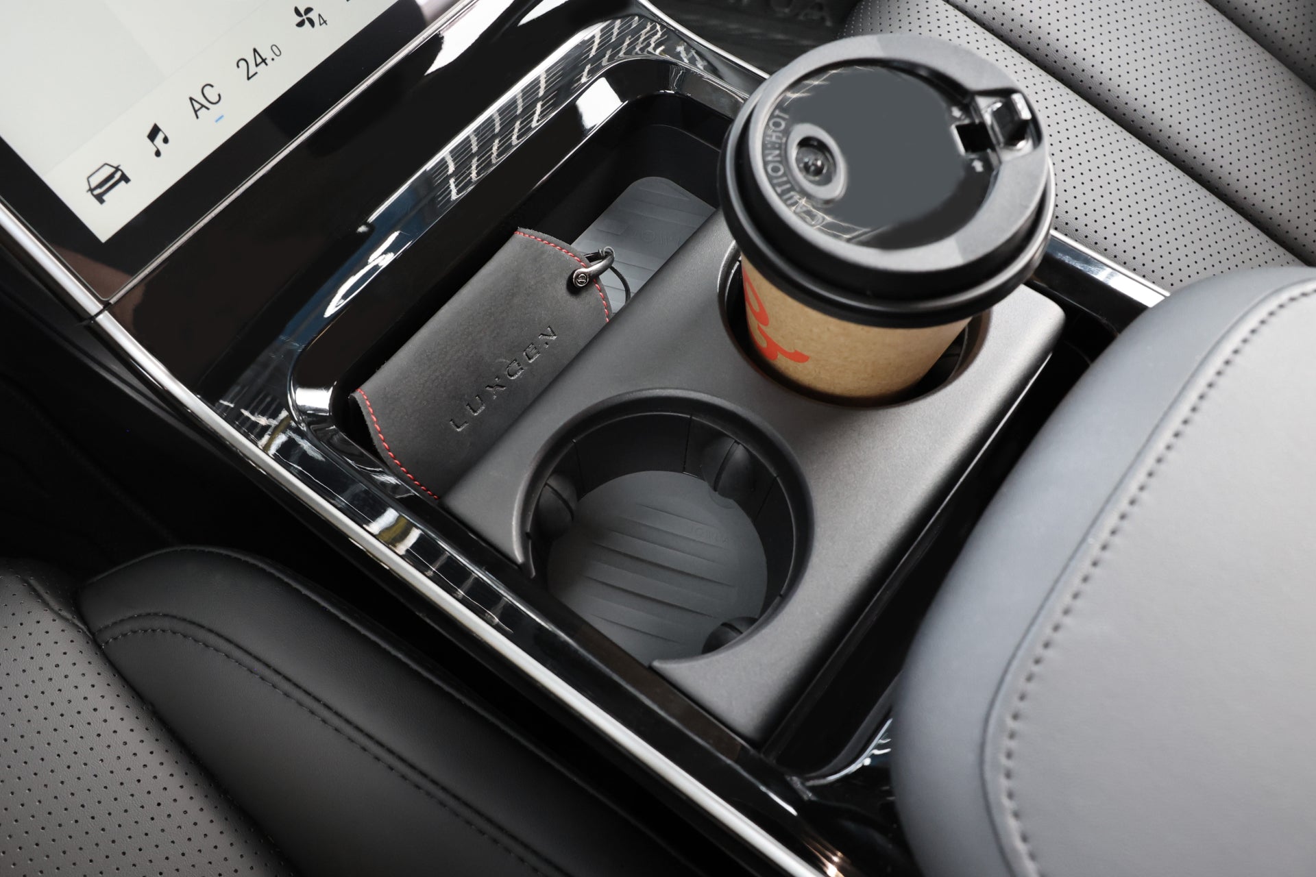 汽車中控台特寫,配有黑色皮革和觸控屏,配有 Luxgen n⁷ 鑰匙圈。 JOWUA 台灣杯架組(LUXGEN n⁷、n⁷ LR)中放置著一個帶有黑色蓋子的杯子,而背景中可以看到穿孔的皮革座椅。.