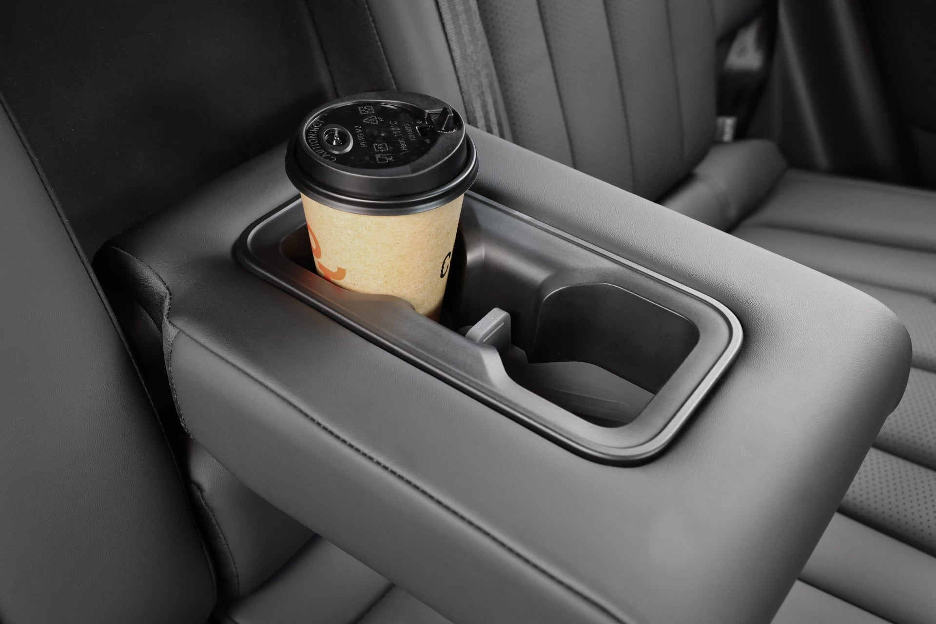 納智捷n⁷後座扶手的杯架組中放置了一個帶有黑色蓋子的JOWUA台灣一次性咖啡杯。內部的深灰色內裝與這些時尚的汽車配件相得益彰。.