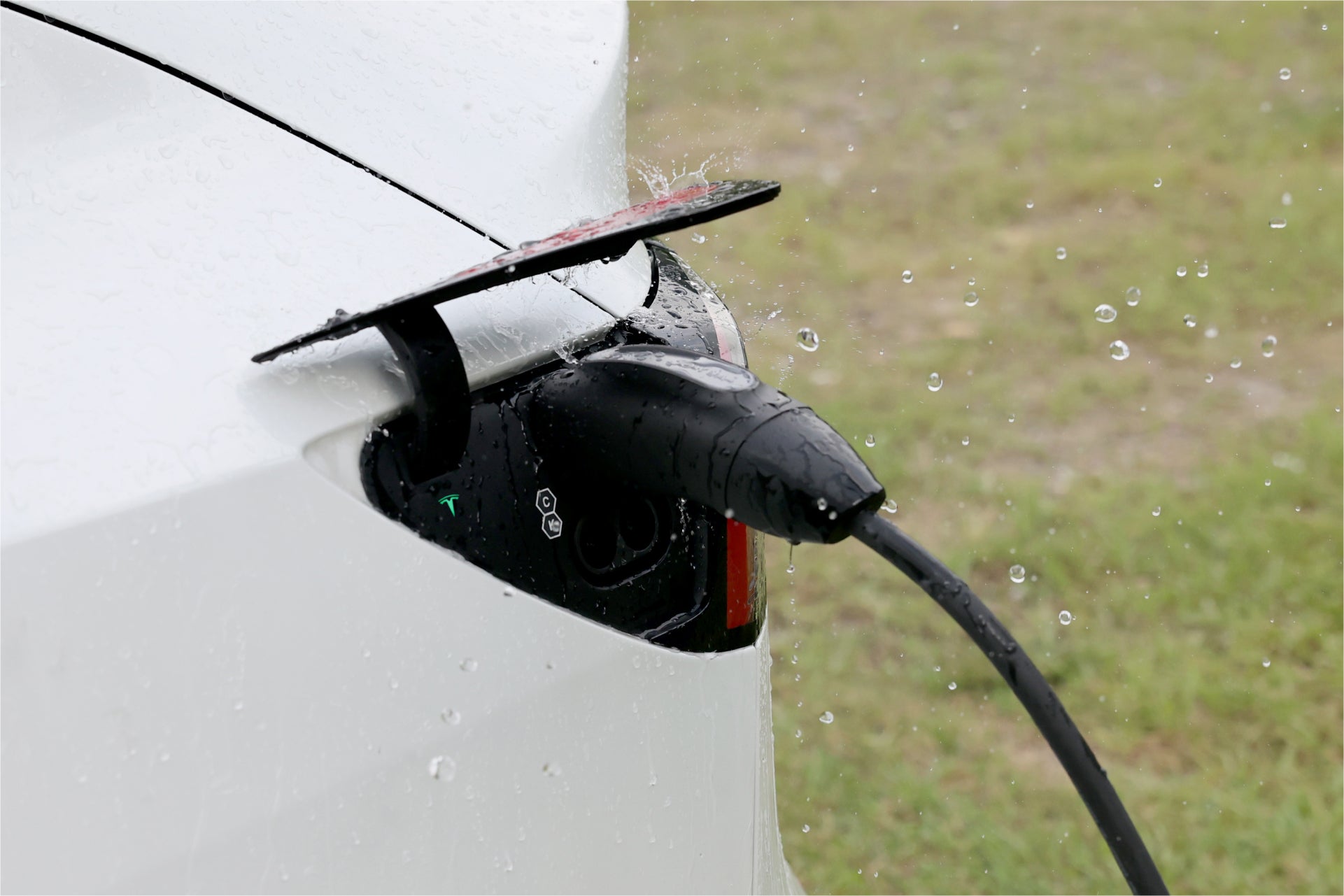 台灣 JOWUA 雙用行動充電器 (CCS2-AC Type-2) 7kW 配備 NEMA 14-50/6-20轉接器組合在雨中為電動車充電的特寫,水滴清晰可見,性能安全可靠。.
