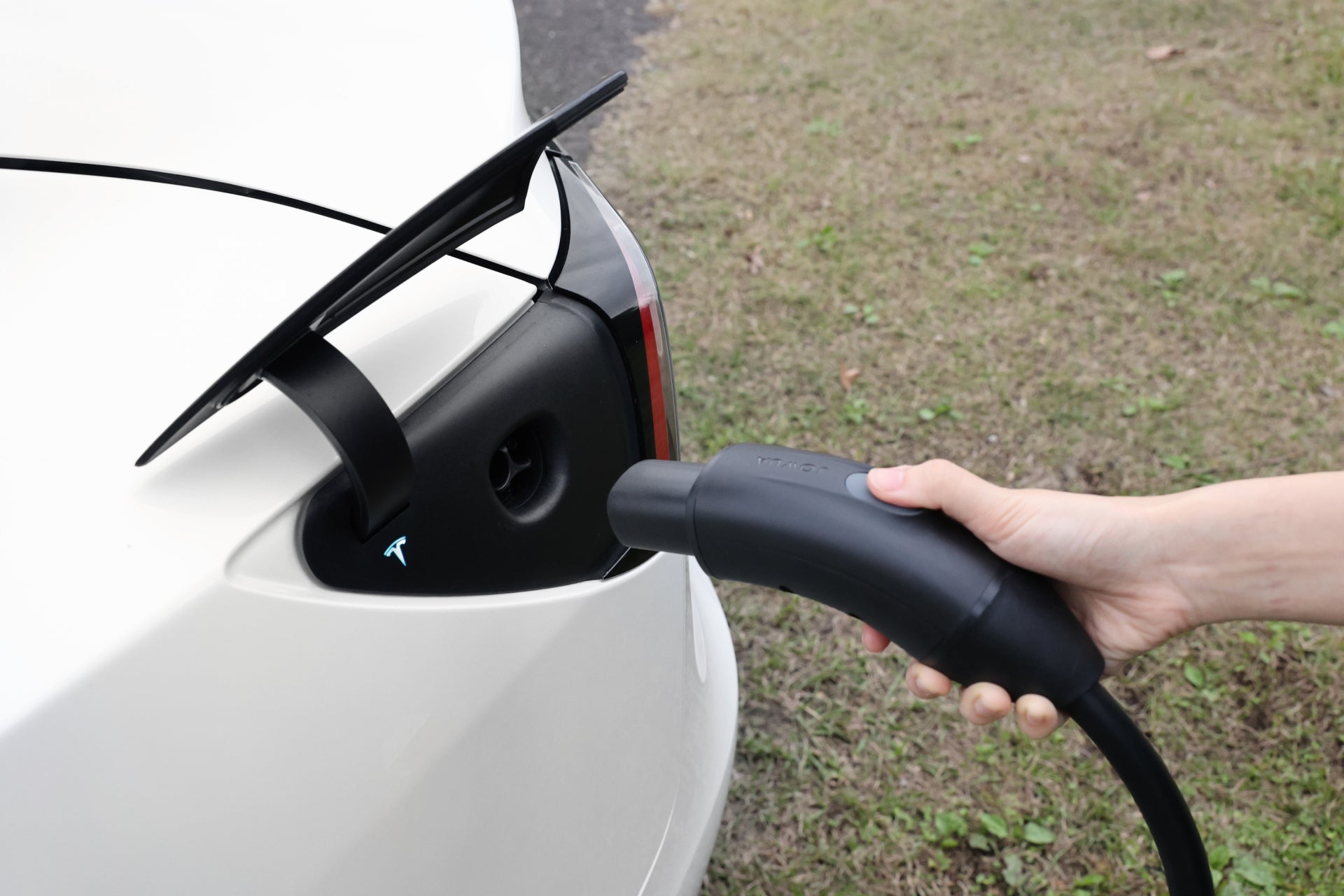 台灣 JOWUA 雙用行動充電器 (TPC/NACS) 9.6kW|NEMA 14-50轉接器組合連接到白色 EV 的特斯拉 TPC (NACS) 連接埠,可提供 40A/9.6kW 卓越充電效能-非常適合在草地上或旅途中的充電需求。.