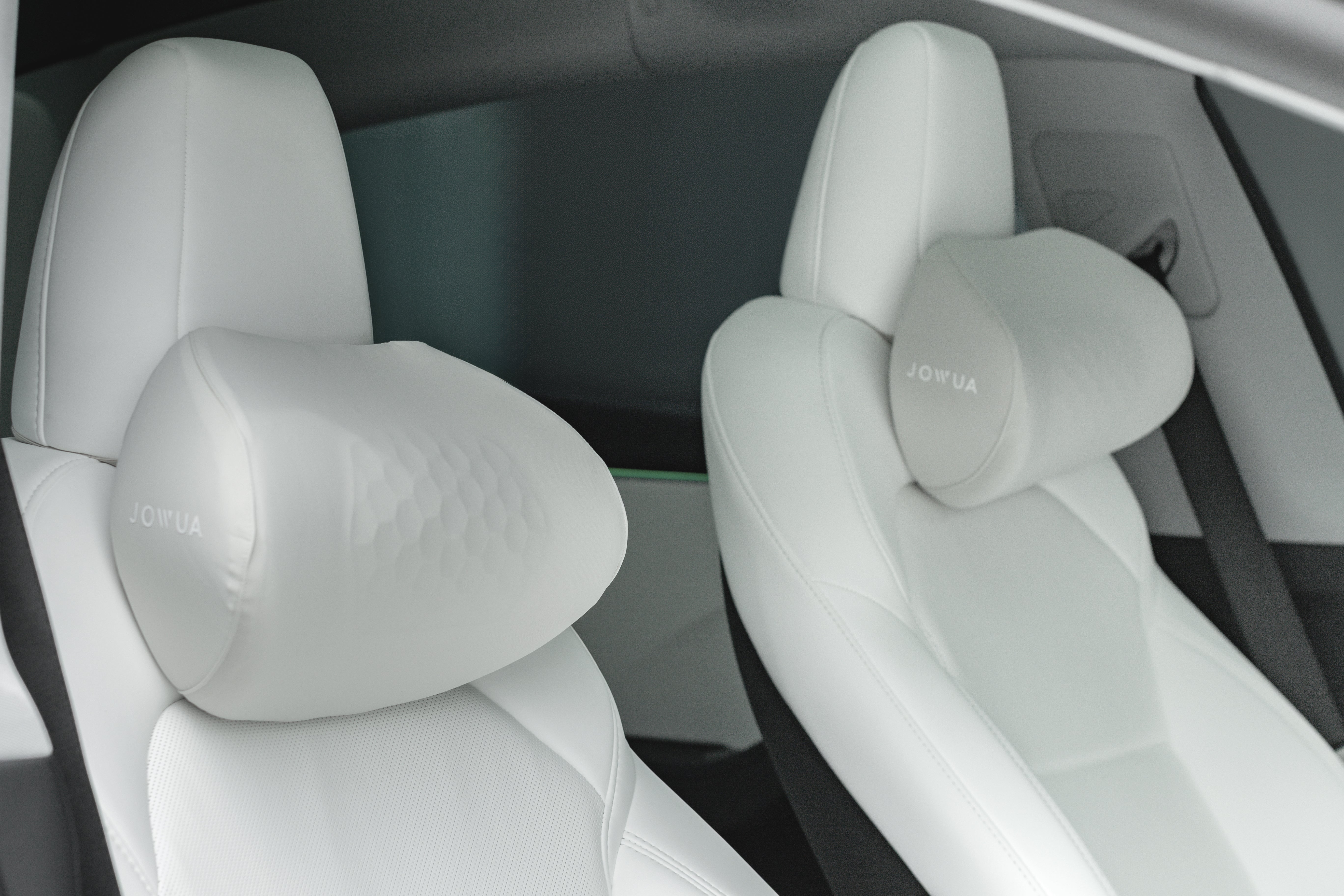Two white car seats with attached JOWUA Taiwan 車用頭枕(兩入)。以人體工學設計和支援性記憶棉為特色,內裝採用時尚、簡約的現代車廂設計。.