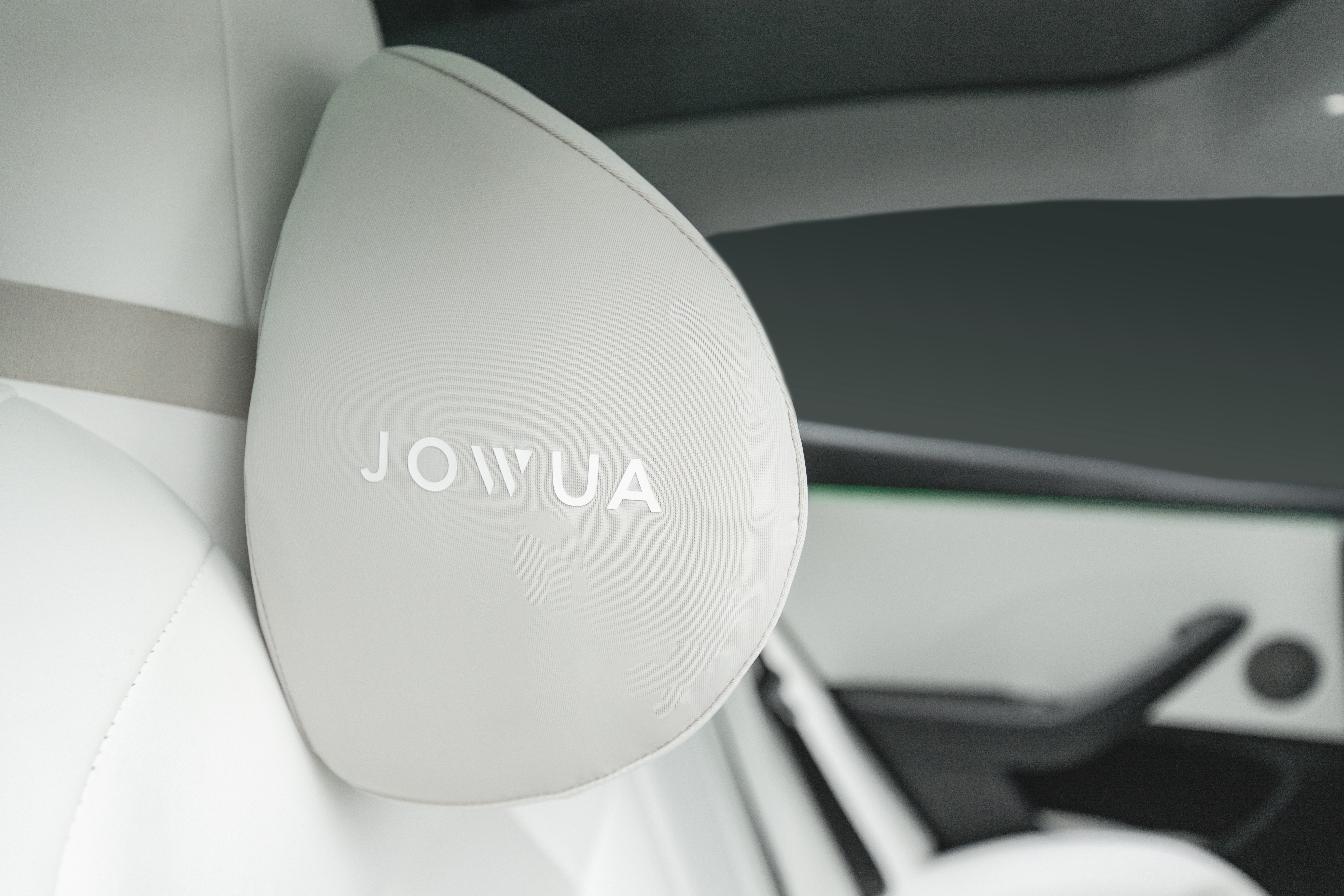 JOWUA Taiwan 車用頭枕(兩入/一入)的特寫。米色布料上的白色字母,貼在現代車輛內的白色真皮汽車座椅上。.
