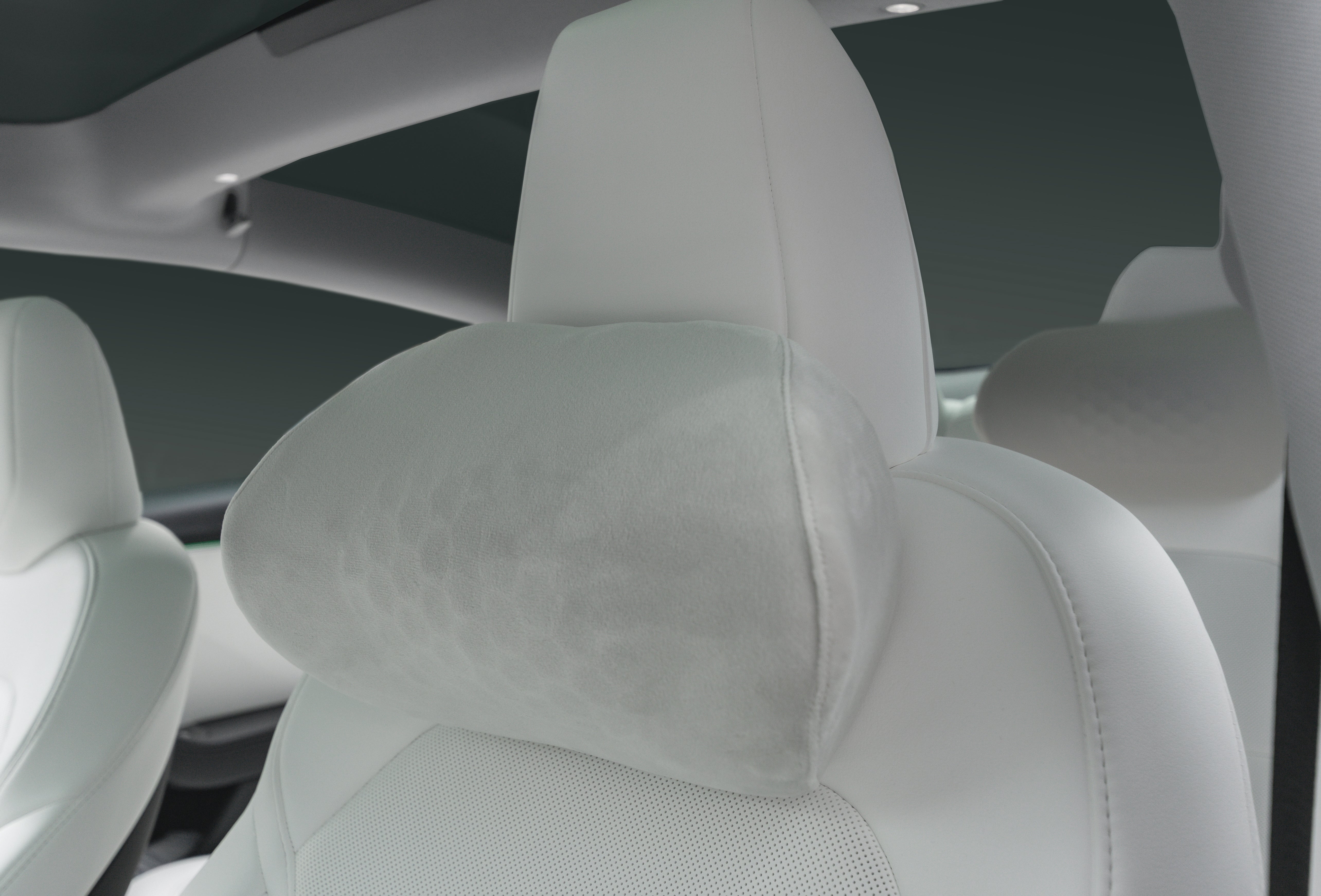 白色車用頭枕(兩入/一入)與淺灰色、柔軟的 JOWUA Taiwan 車用頭枕(兩入/一入)的特寫。附在頭枕上。背景可見車內裝潢與深綠色車窗。.