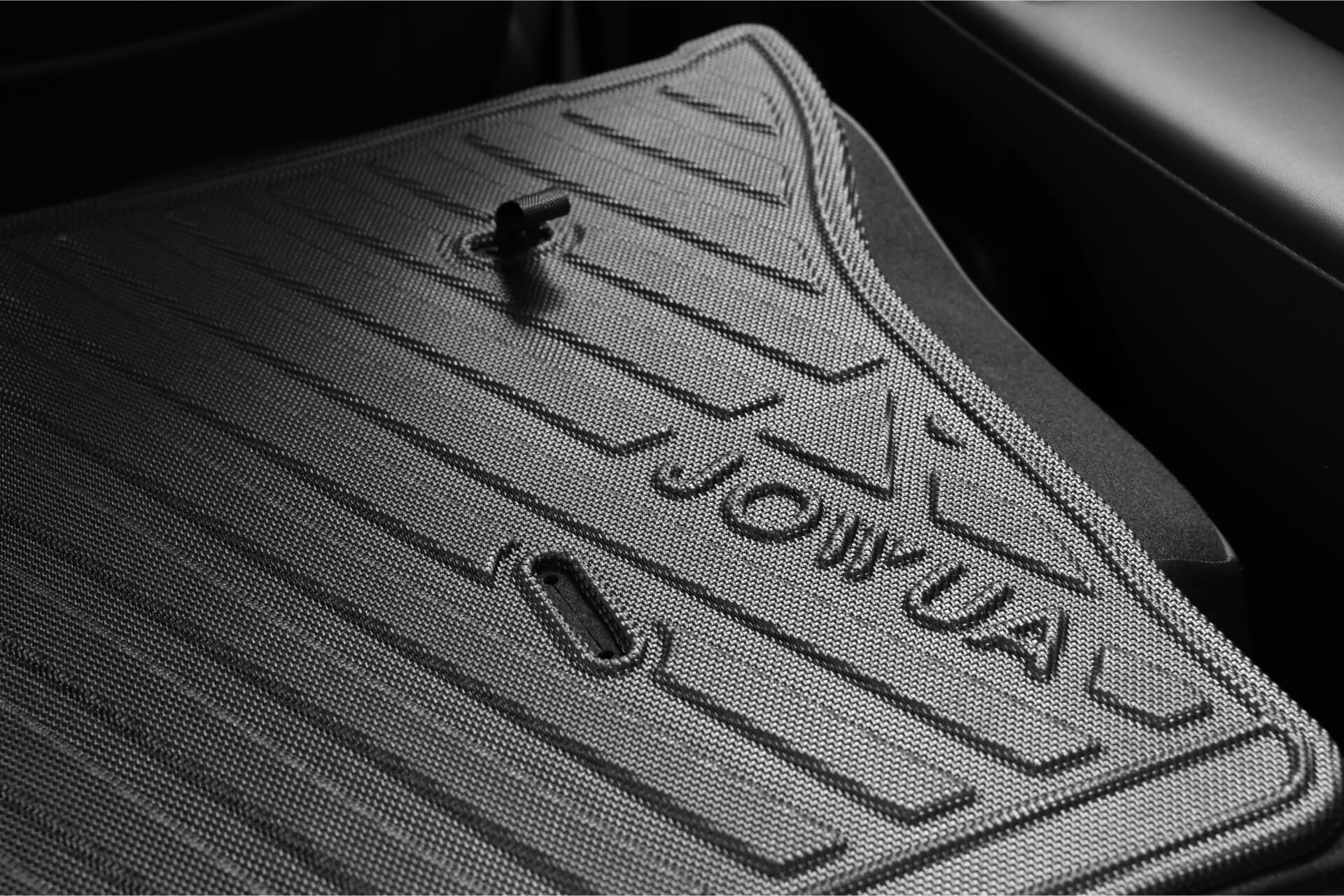 來自台灣JOWUA的LUXGEN n⁷汽車腳踏墊特寫,採用透明防水TPE材質製成,具有紋理羅紋設計、凸起圖案和「JOWUA」壓紋。在燈光亮點中可以看到固定夾。.