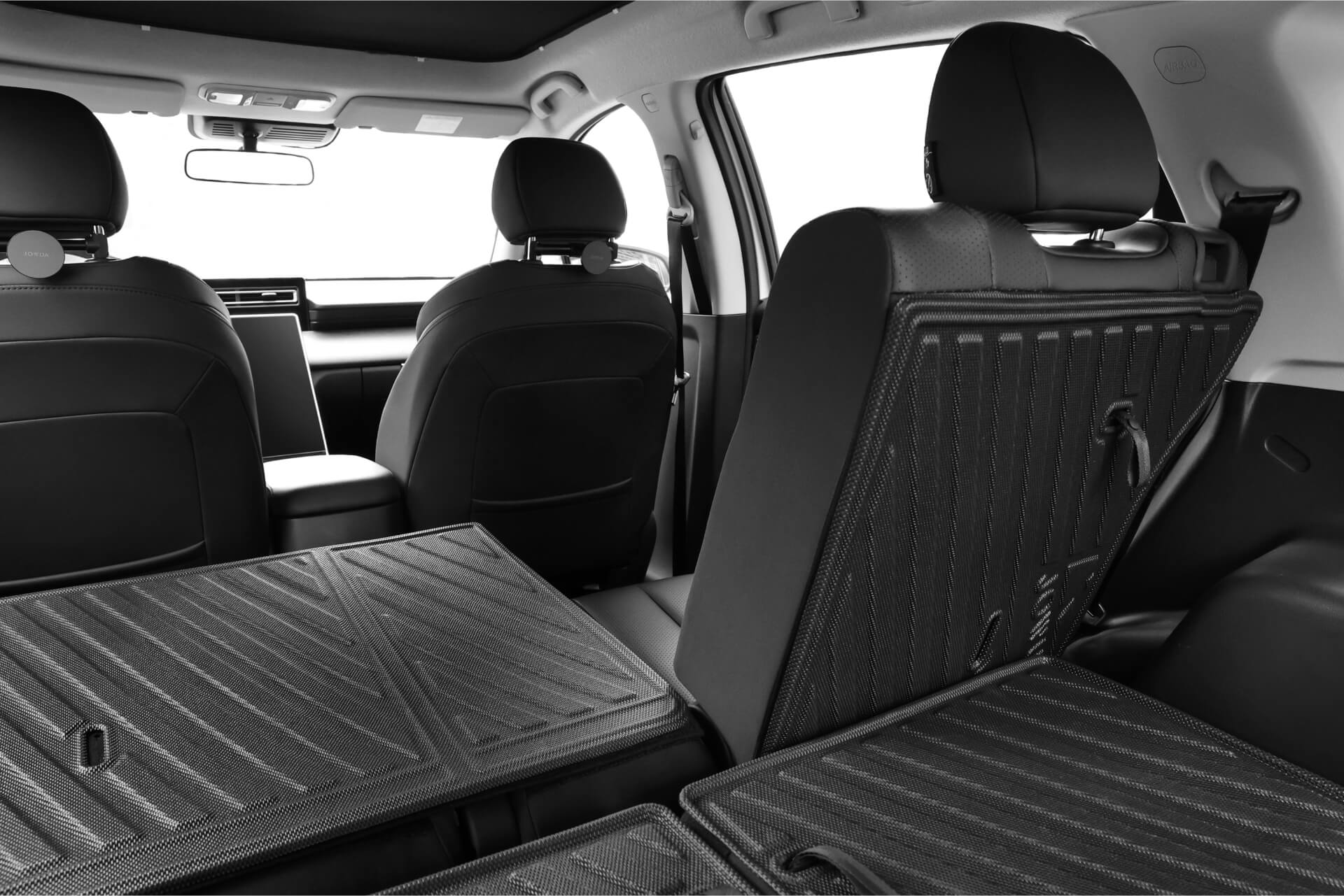 LUXGEN n⁷ 7 人座車中的 JOWUA 台灣防水第二排椅背墊的內部視圖顯示後座折疊以提供額外的載貨空間,突出顯示黑色內飾、現代設計元素和保護性 TPE 材質。.
