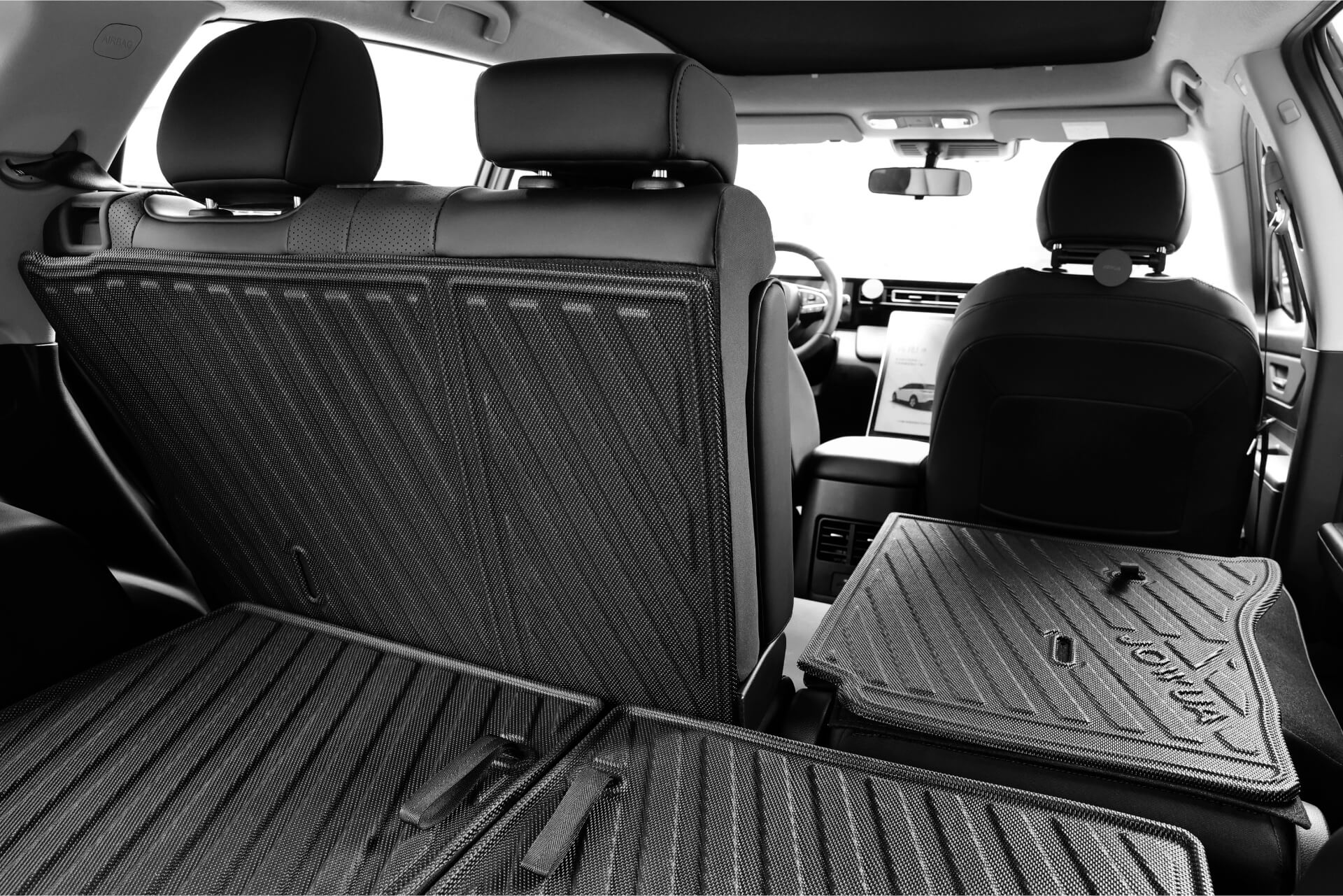 JOWUA 台灣 LUXGEN n⁷ 的內部視圖,展示後座。 防水第二排椅背墊座椅向下折疊以擴大貨物空間,並強調防水功能。儀表板和前排座椅採用黑白顏色,突出了細節和紋理。.