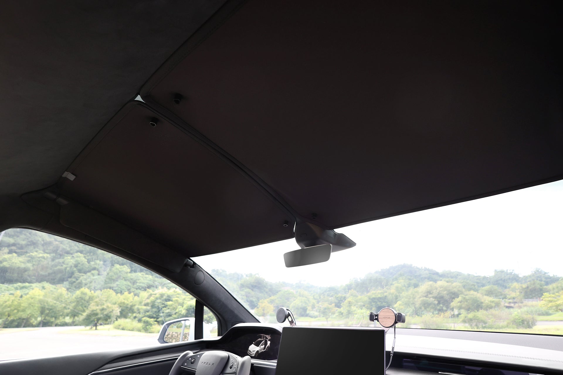 JOWUA Taiwan 的分離式遮陽簾 (Model X),從車內觀察車頂和擋風玻璃。後視鏡、裝載螢幕的儀表板和電話座,以及車外的樹木和山丘都清晰可見。.