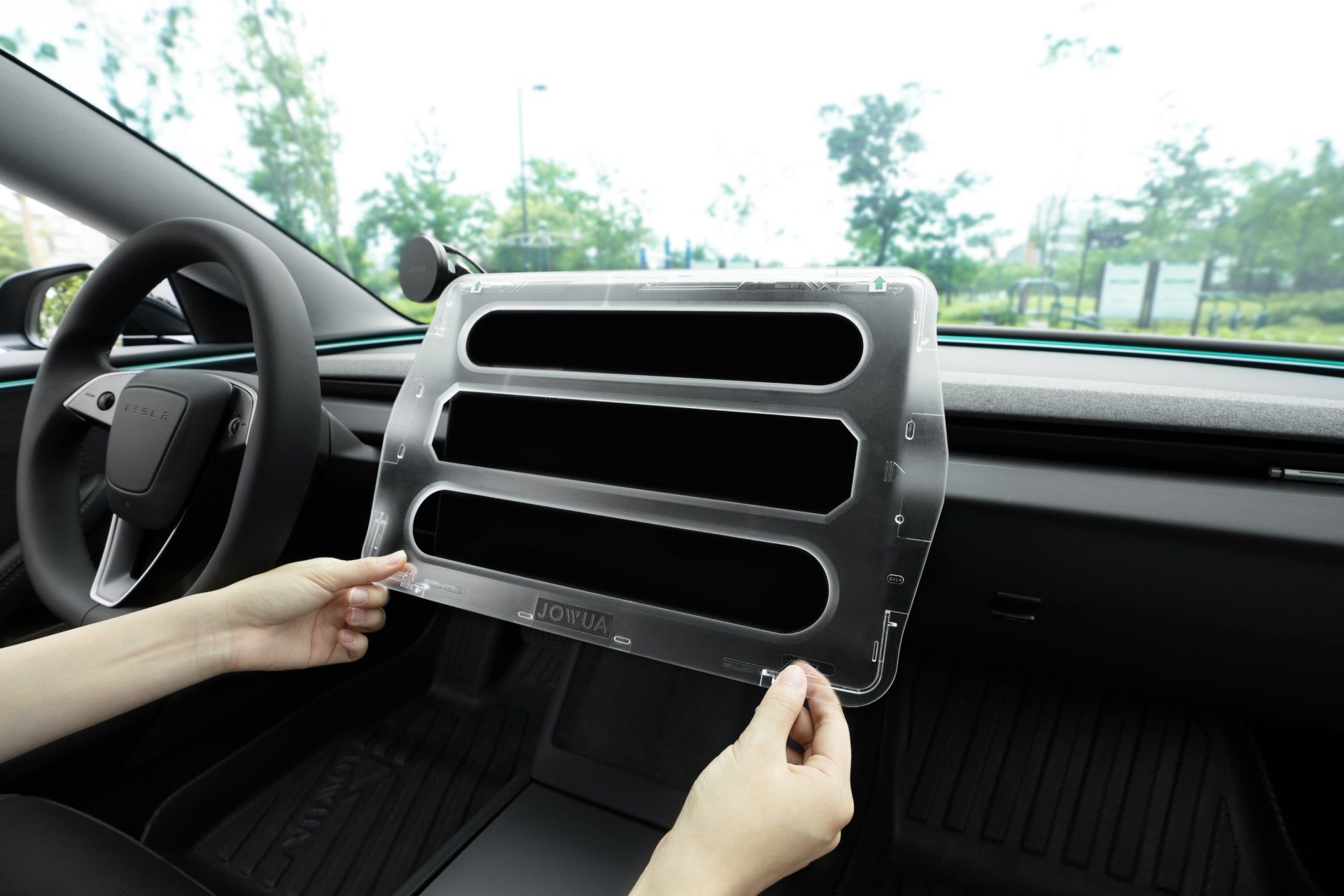 將 JOWUA Taiwan 一幕瞭然【Model 3 煥新版|交車禮包】air vent cover 安裝於 Tesla Model 3 車內,將其對齊儀表板通風口,車內與車外樹木清晰可見。.