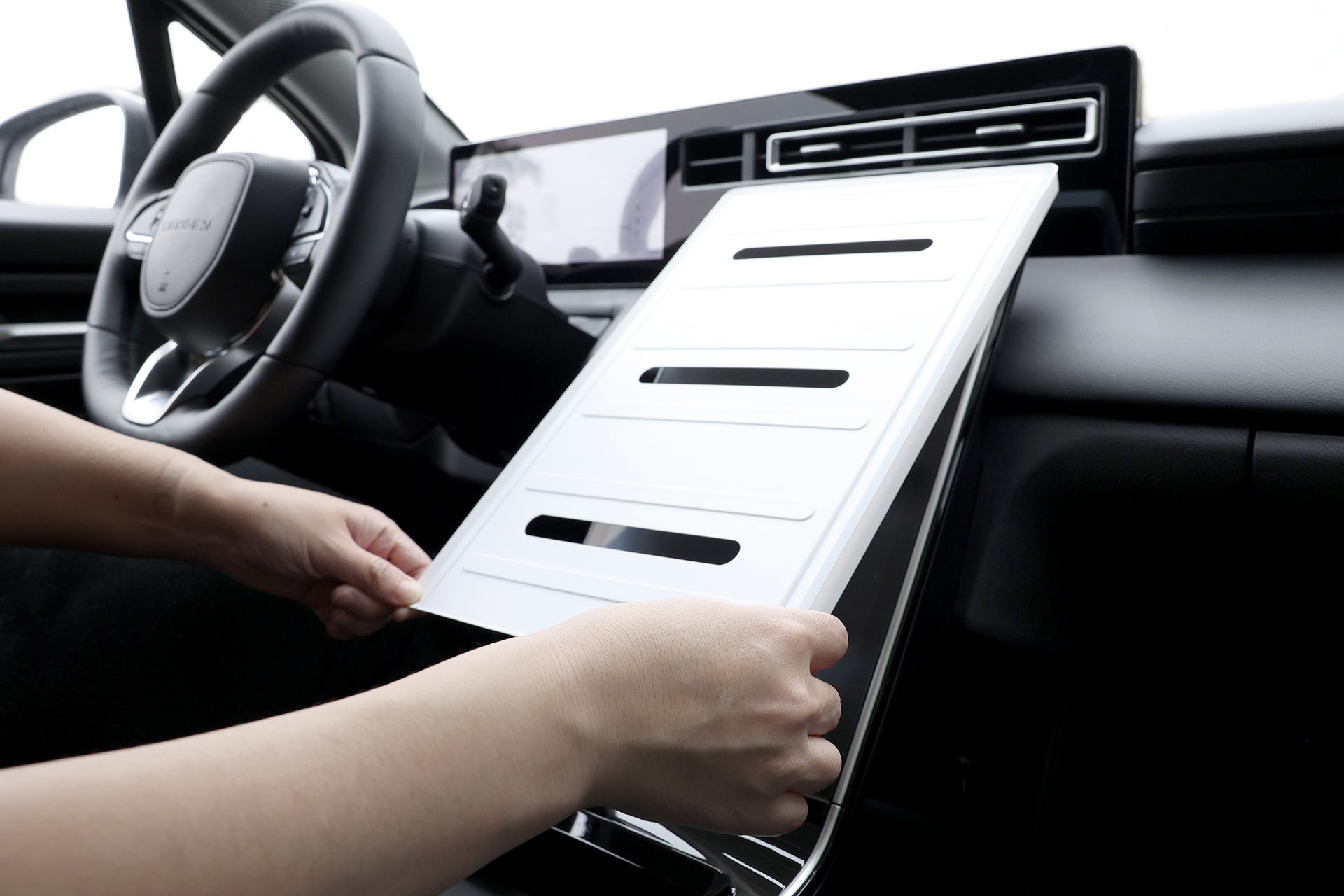一個人正在從 LUXGEN n⁷ 儀表板隔間中插入或取出矩形空氣過濾器。這款現代車輛的光滑內飾展示了方向盤和數位螢幕,可能採用 JOWUA 台灣 9H 硬度的玻璃屏幕保護貼進行保護,以獲得最佳清晰度。.