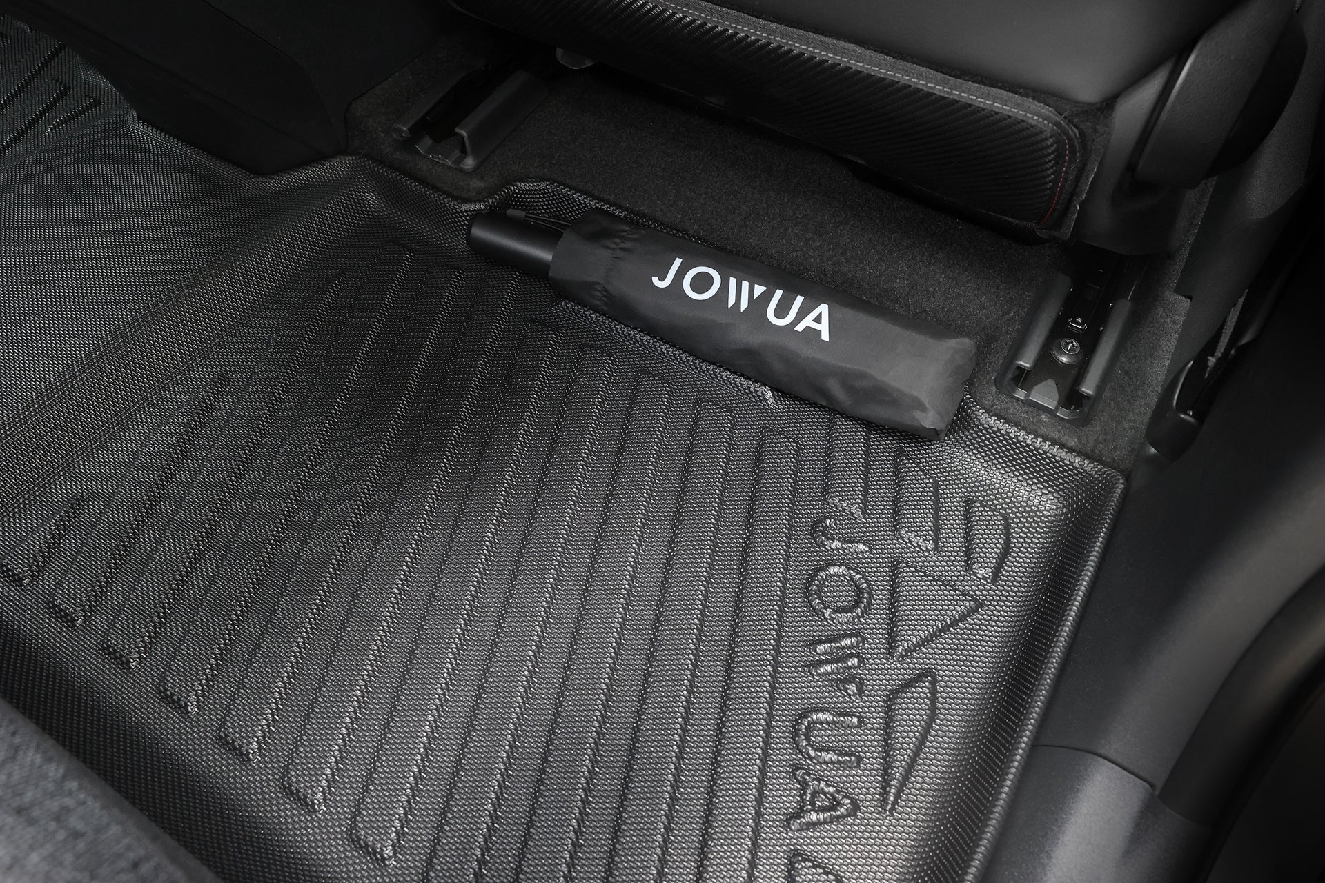 這張特寫照片展示了 JOWUA 台灣 立體防水腳踏墊(Toyota bZ4X),其表面帶有紋理圖案並印有 JOWUA 標誌,突顯其「全面防護車墊」的設計。 旁邊是一只黑色 JOWUA 專利汽車收納袋,整齊地收納在車座下方。.