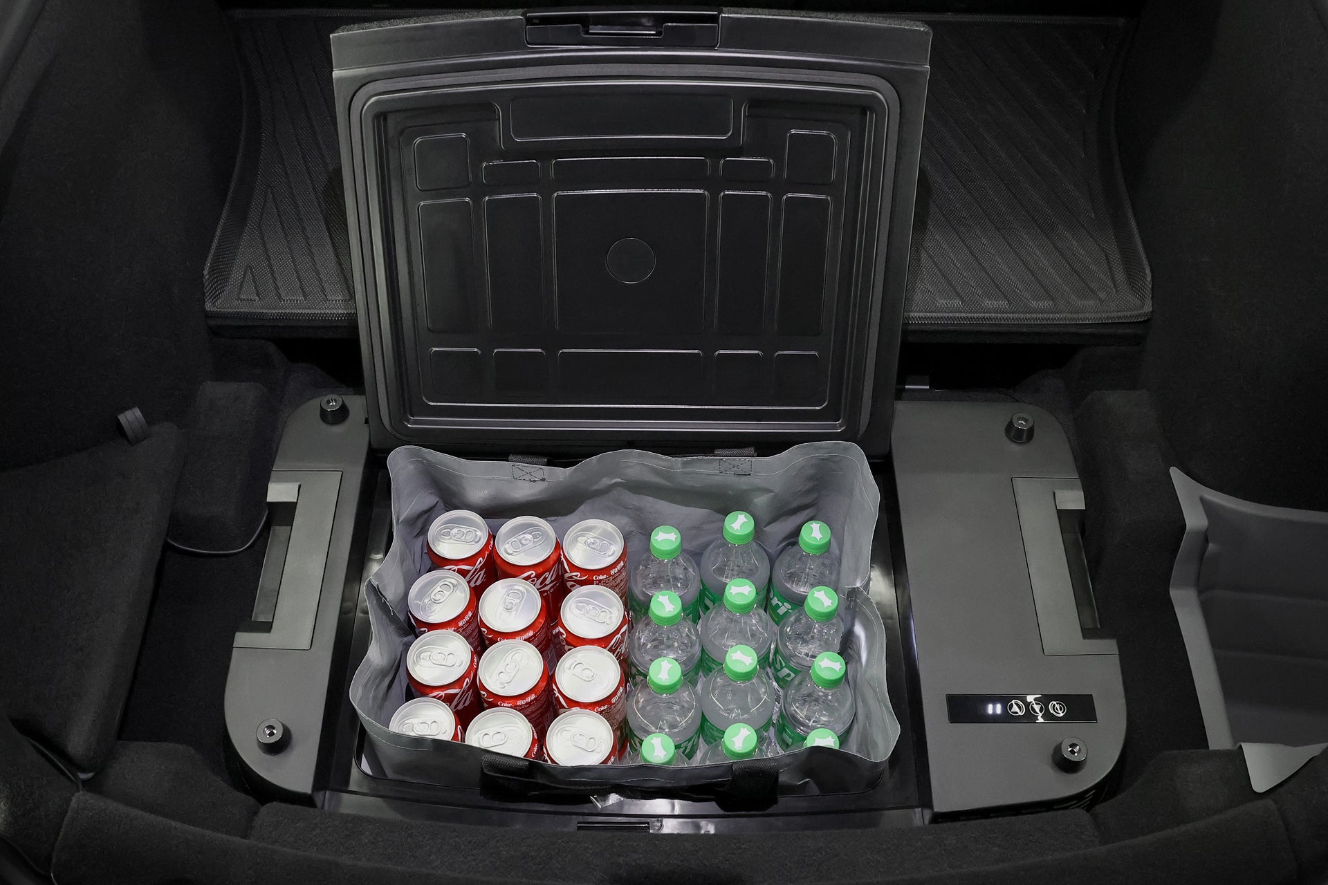 汽車後備箱裡放著 JOWUA Taiwan Type-C & 點菸器 雙軌車用行動冰箱 (Model Y全車系),打開冰箱蓋,可以看到寬敞的隔間裡整齊地冷藏著一罐罐汽水和一瓶瓶清水。.