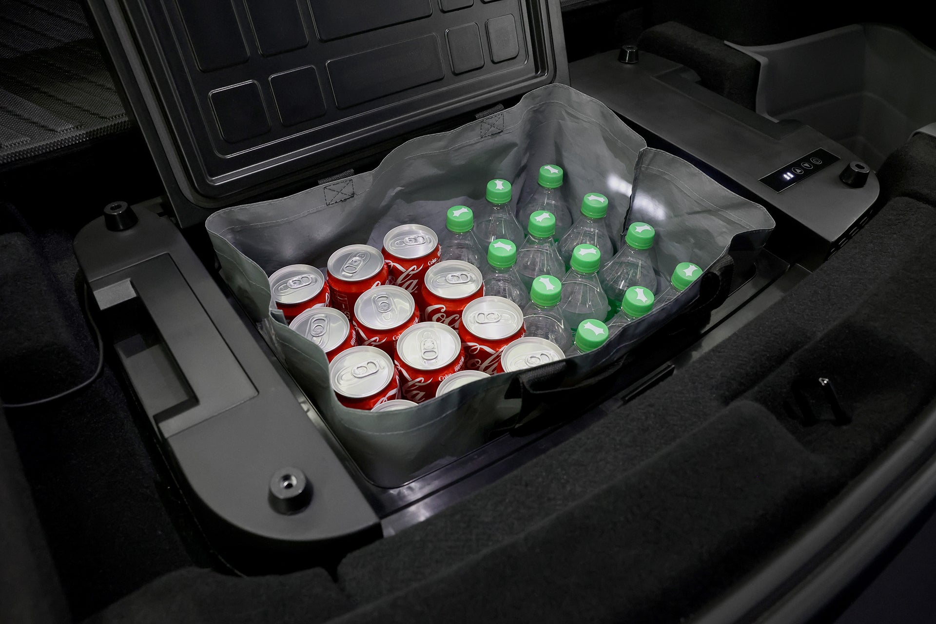 一輛 JOWUA Taiwan Type-C 車用行動冰箱 (Model Y 全車系) 放在汽車後備箱中,整齊地包裝著罐裝汽水和塑膠水瓶,有些瓶蓋還是綠色的。.