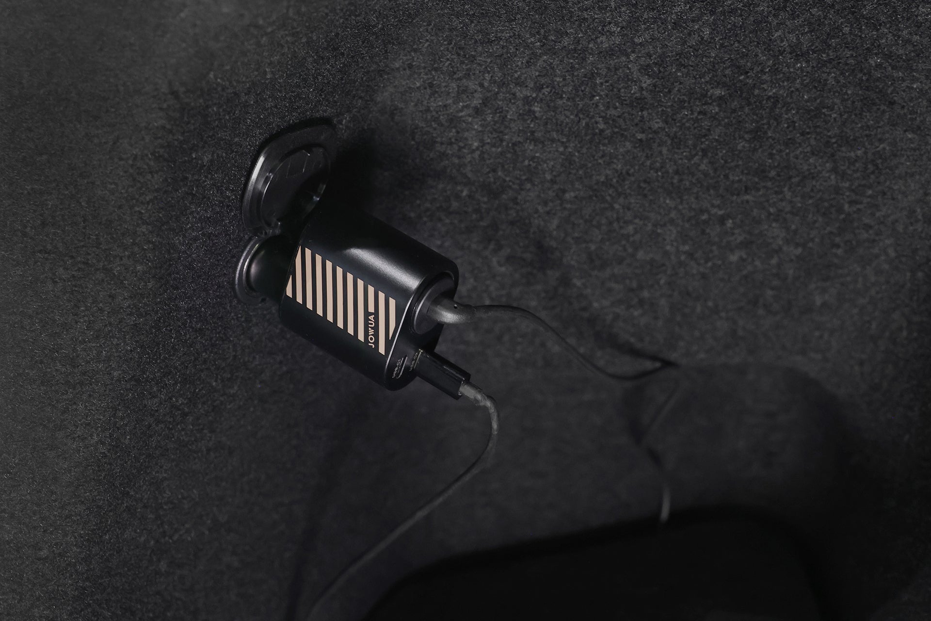 深色地毯上的 JOWUA 台灣 Type-C & 點菸器 雙軌車用行動冰箱 (Model Y 全車系) 特寫,透過 Type-C 連接線插入,橫向條紋和小標籤清晰可見。.