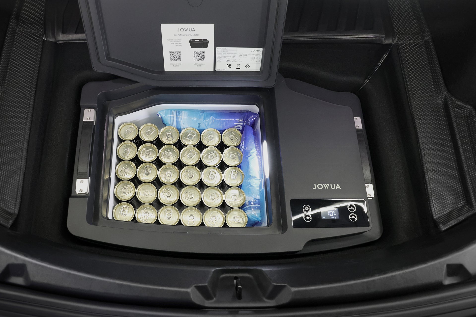 汽車後備箱內有一台 JOWUA 台灣 Type-C 車用行動冰箱 (Model 3 全車系),打開蓋子,可以看到裡面整齊排列的罐頭和冰塊。這款冰箱採用數位控制面板和 Type-C 供電系統。.