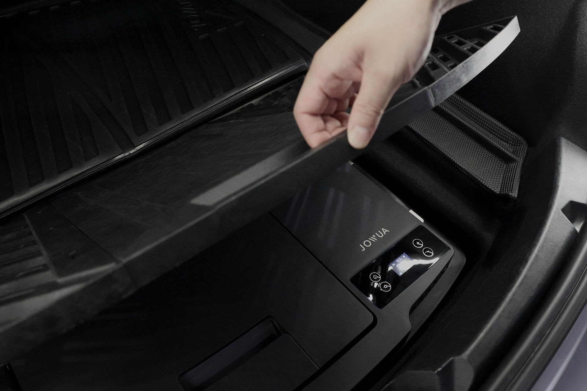 一隻手掀開汽車後備箱蓋,露出 JOWUA 台灣 Type-C 車用行動冰箱 (Model 3 全車系),配備數位顯示器和按鈕,是高效率電源供應器的理想選擇,也可讓您的物品在旅途中保持低溫。.