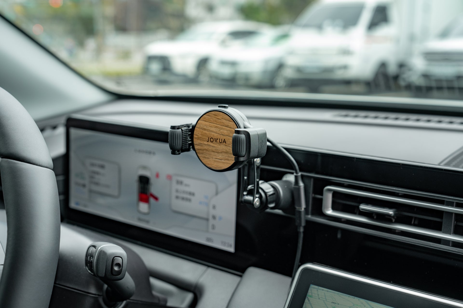 該車的內裝採用了JOWUA台灣出風口車架Qi2(滿輪款),這是一款木質飾面的手機支架,與無線網路充電無縫整合。附近的觸控螢幕顯示導航和設定。透過擋風玻璃,您可以看到城市景觀中的多輛車輛。.