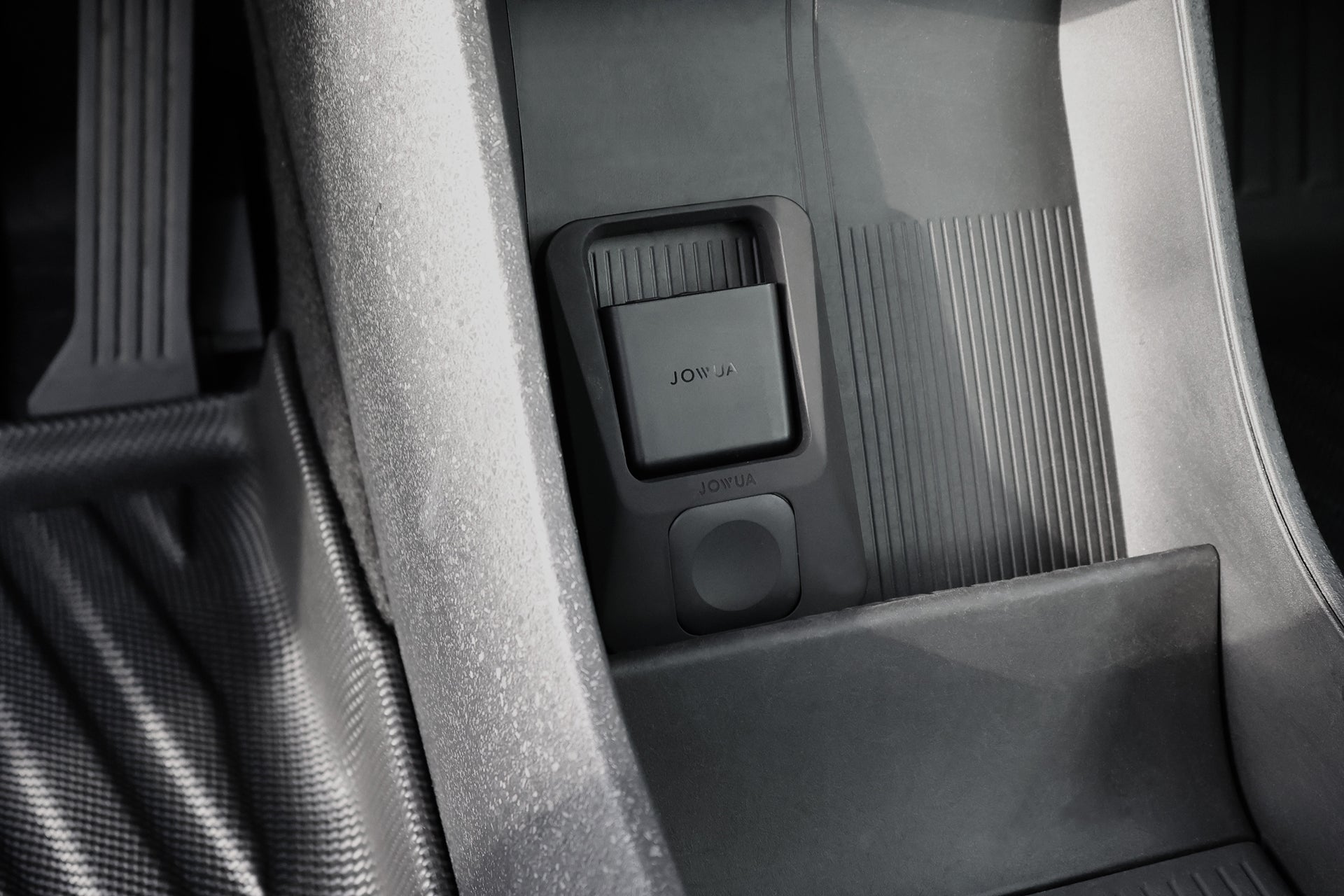 汽車內裝特寫,深色的 JOWUA Taiwan GPS 護盾安裝在中控台與座椅之間。光線與陰影突顯其紋理細節。.
