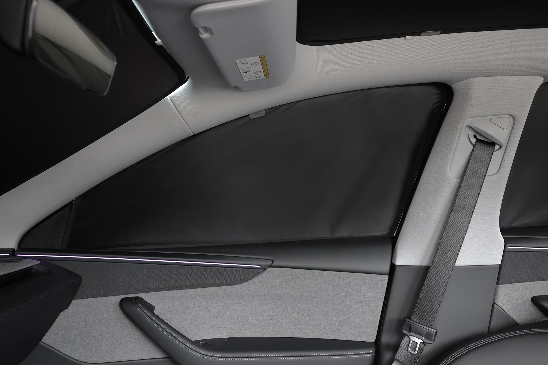 圖為汽車後座區域的內部側視圖,其特色包括安全帶、Model Y (2021-2025+) 的 JOWUA Taiwan 全車終極遮陽組合窗簾、灰色紋理門板,以及沿著車門飾板的微妙環境照明。.