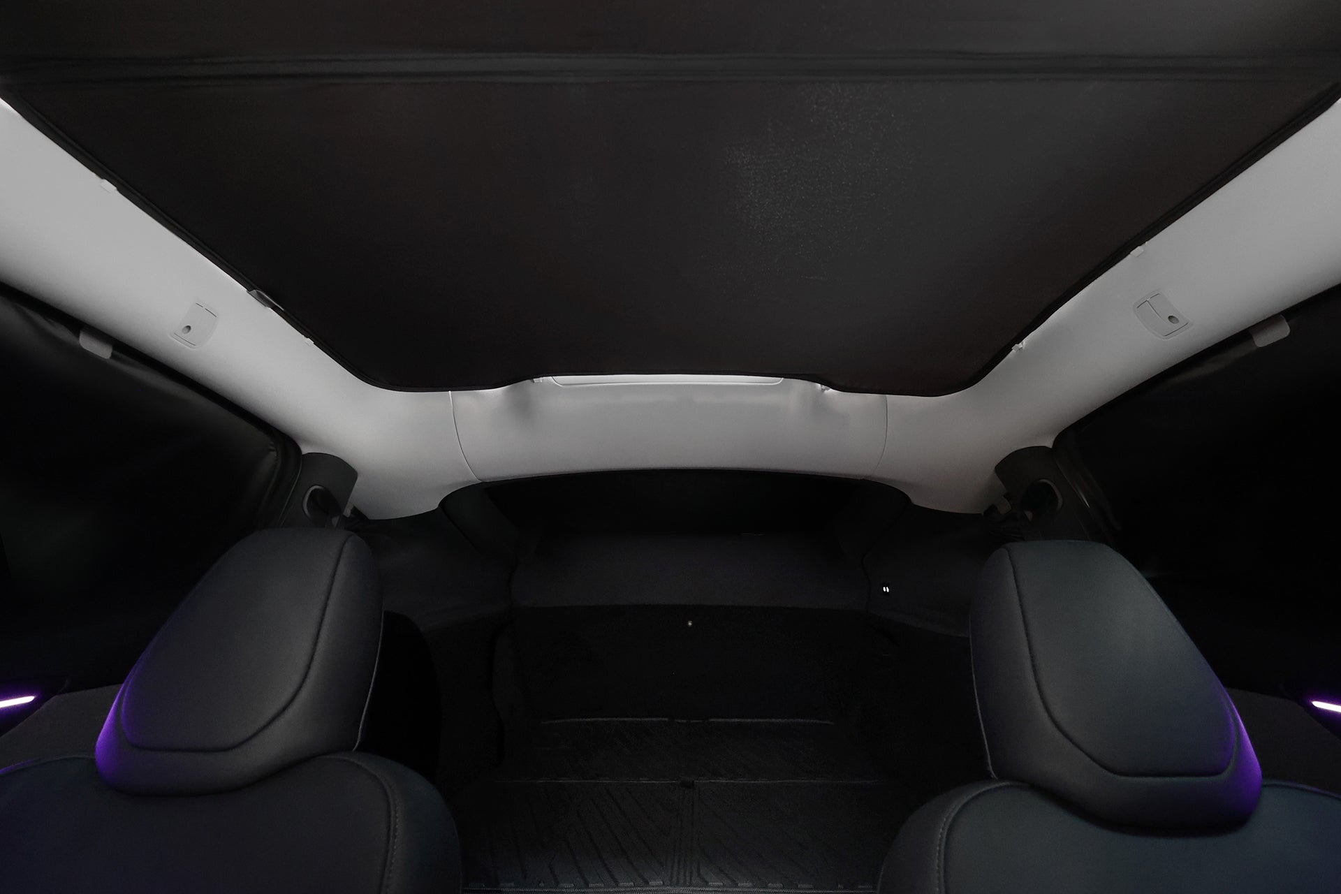 車內景觀:兩個黑色前座,配備 JOWUA Taiwan 全車終極遮陽組合 (Model Y 煥新版 2025+/2021-2024) 的大型全景玻璃車頂,部分收起可達 99% 抗 UV 防曬隔熱隱私,後方貨運區有柔和的環境照明。.