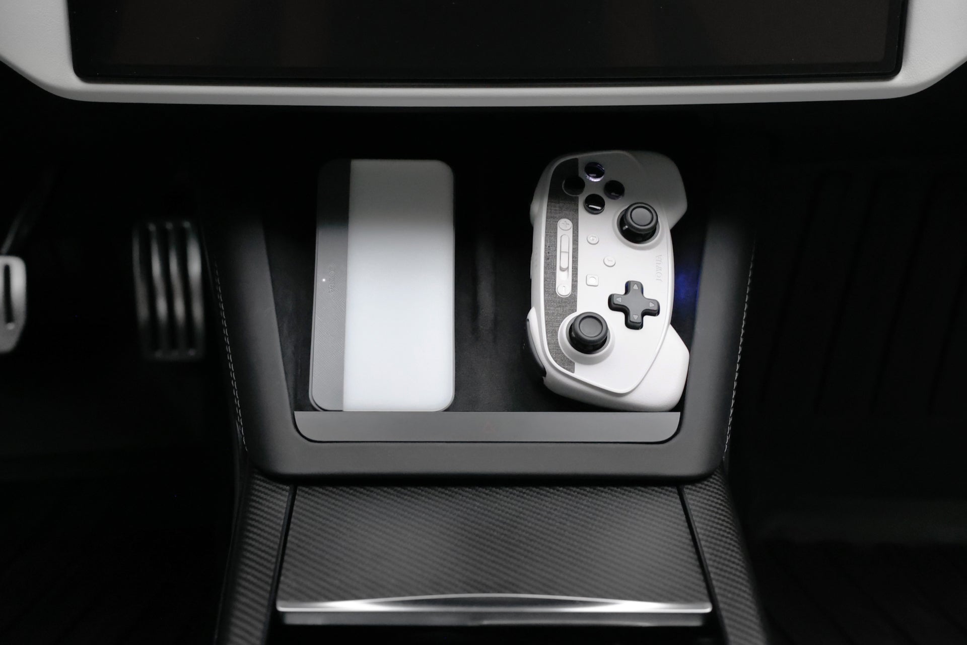 特寫圖顯示 JOWUA Taiwan 無線充電雙搖桿組合(Model 3/Y)與長方形觸控板放在汽車中控台上;背景出現踏板,暗示 Switch 2 支援車內遊戲。.