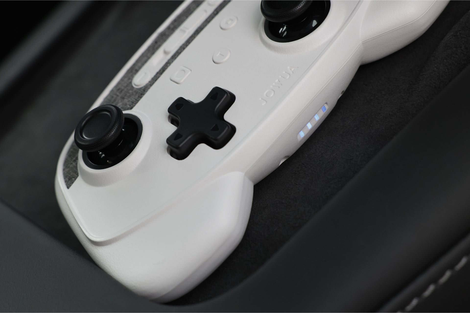 JOWUA Taiwan 無線充電雙搖桿組合(Model 3/Y)的特寫,採用白色設計,搭配黑色按鈕和搖桿、紋理手柄和照明指示燈,放置在深色布料表面上。.