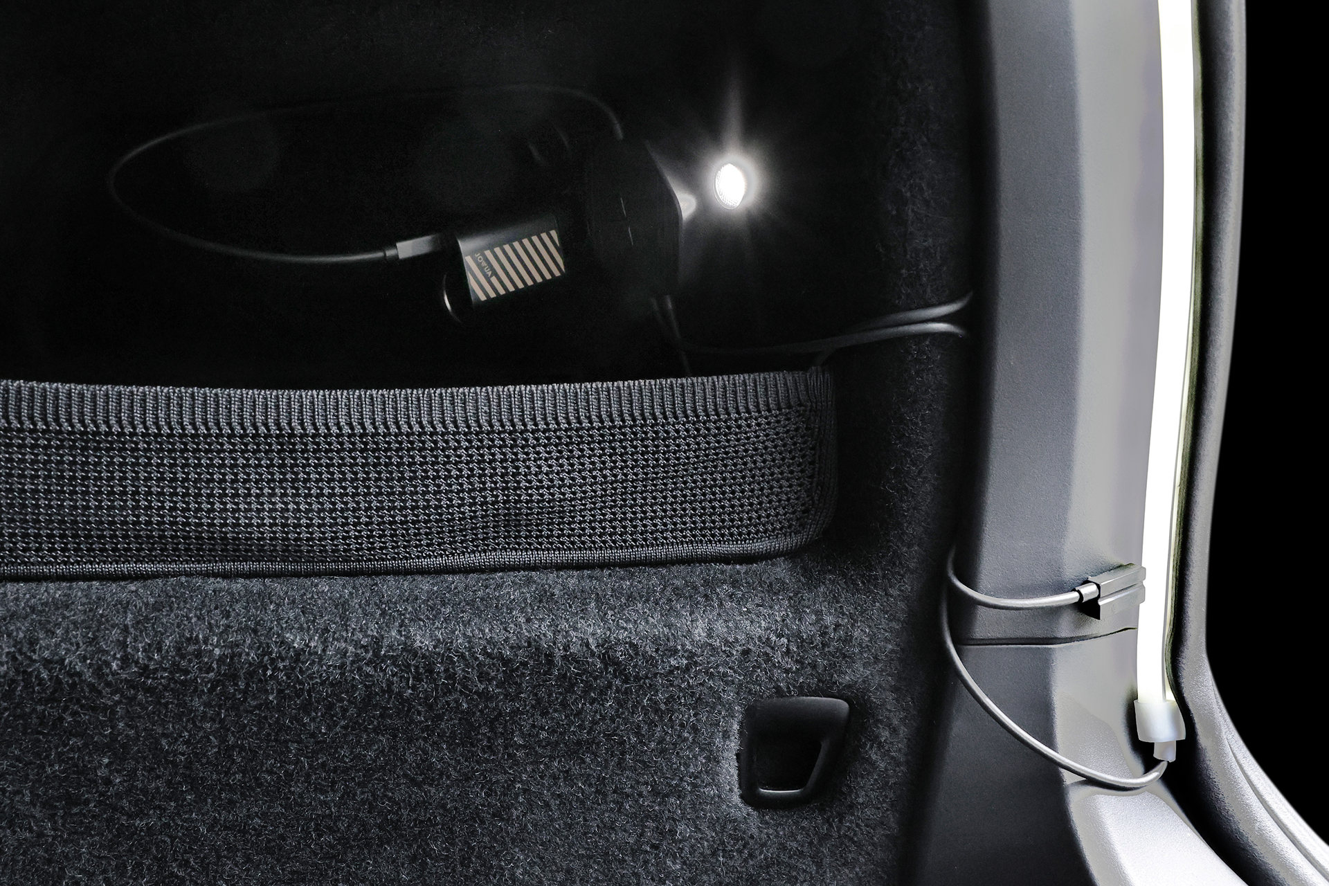 特寫圖顯示 JOWUA 台灣後車廂氣氛燈|真言套索 (Model X) 置於汽車後備箱中,以 Type-C 擴充點菸器供電,連接線沿著邊緣,下方則是網狀收納袋。.