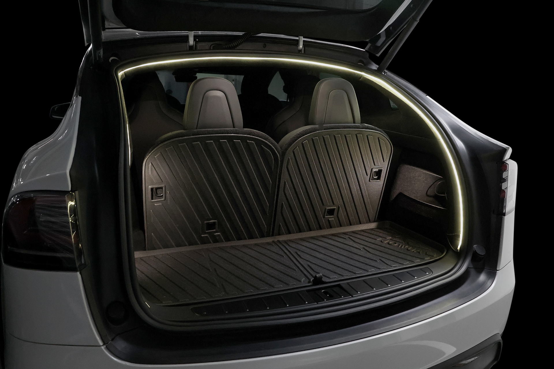 一輛白色 SUV 的開放式後車廂,邊緣鑲有 JOWUA Taiwan 的後車廂氣氛燈|真言套索 (Model X),照亮保護墊和後排座椅,而 smart Type-C 擴充點菸器則增添便利性。.