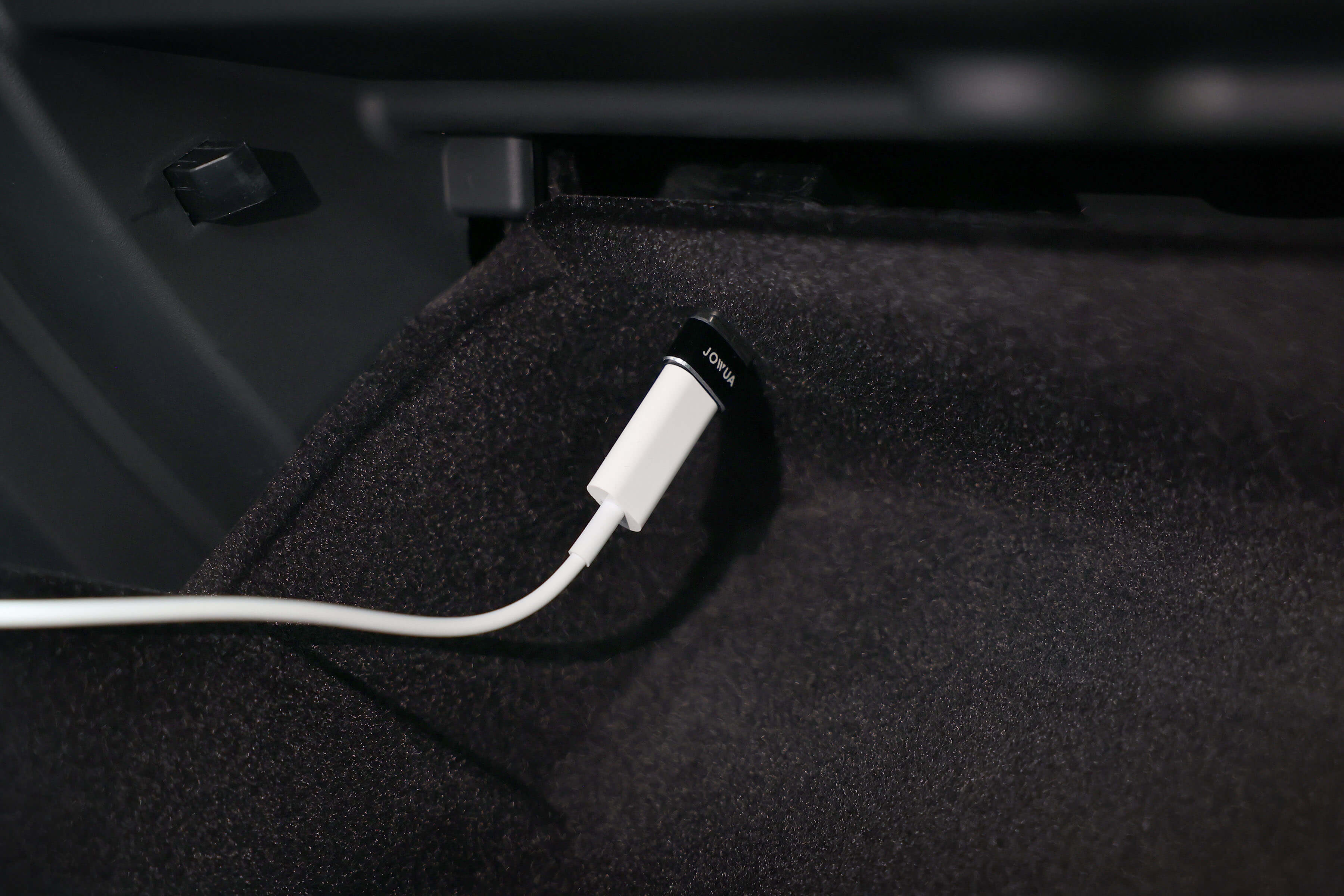 特寫:白色 JOWUA 台灣 Apple Watch 充電套件線插入汽車的“音頻”端口,周圍是深色耐用織物。.