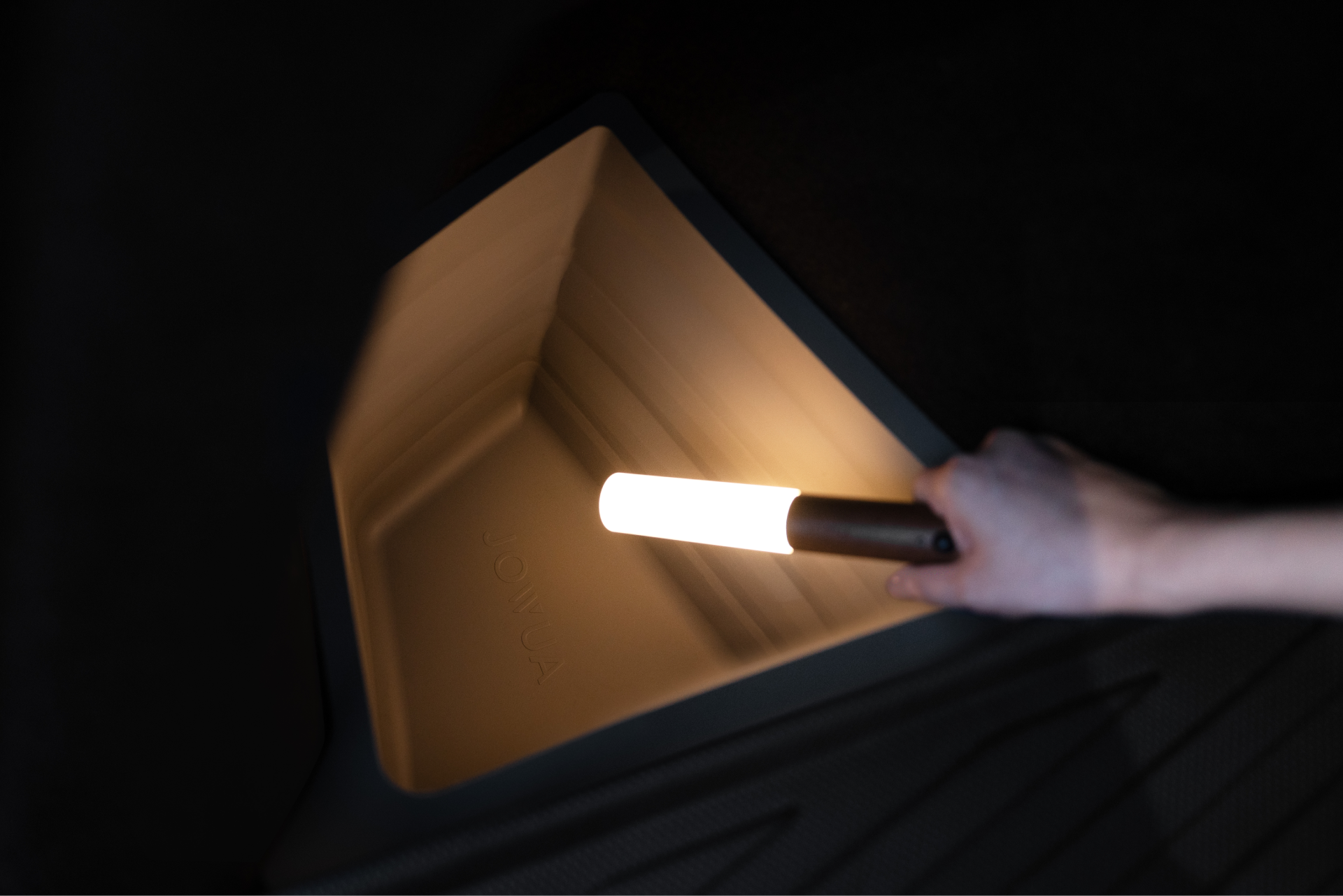 一手握住 LED 感應燈,照亮底部有「SONUA」字樣的深空塑膠箱,非常適合您的 JOWUA 台灣後行李箱收納組(型號 Y 2021-2024)。.