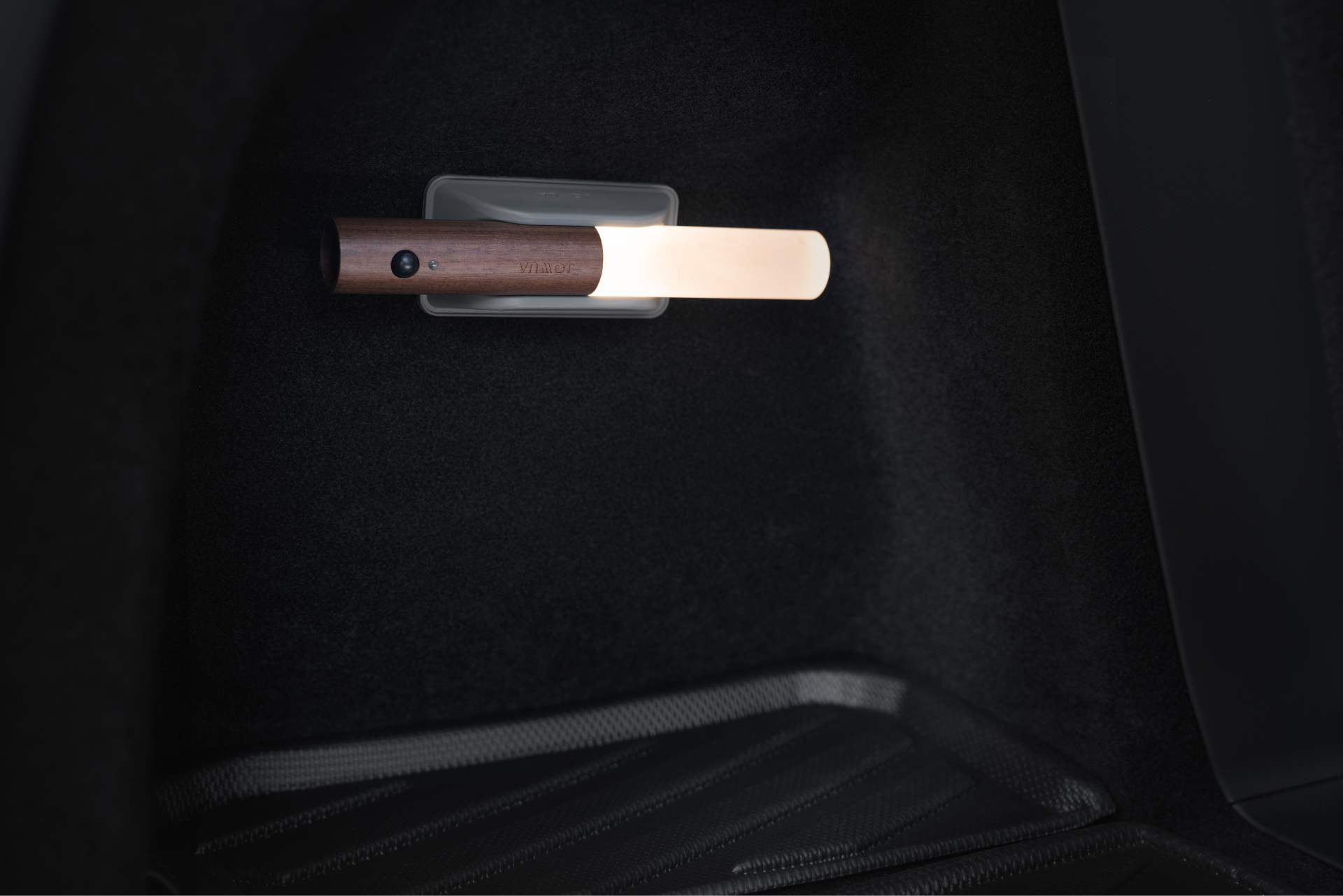 木質圓柱形的JOWUA台灣LED感應燈座安裝在深色牆壁上,照亮了昏暗的空間。下方的紋理地板在燈光下投射出柔和的陰影,而其便利充電功能確保了易於使用。.