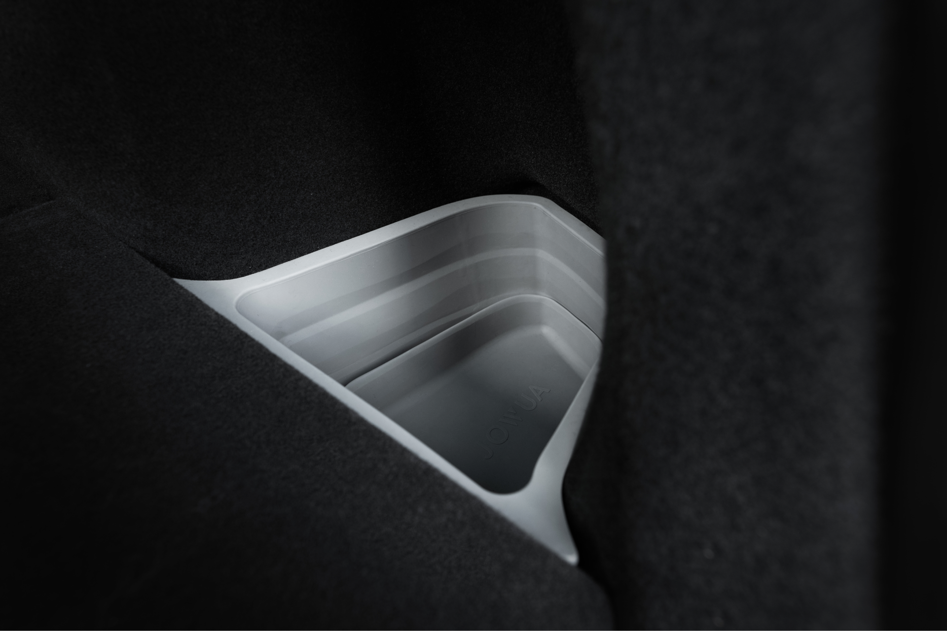 JOWUA 台灣後行李廂收納組(型號 Y 2021-2024)在汽車黑暗內部的特寫。淺灰色的收納盒側面光滑,與深色的內部形成鮮明對比。.