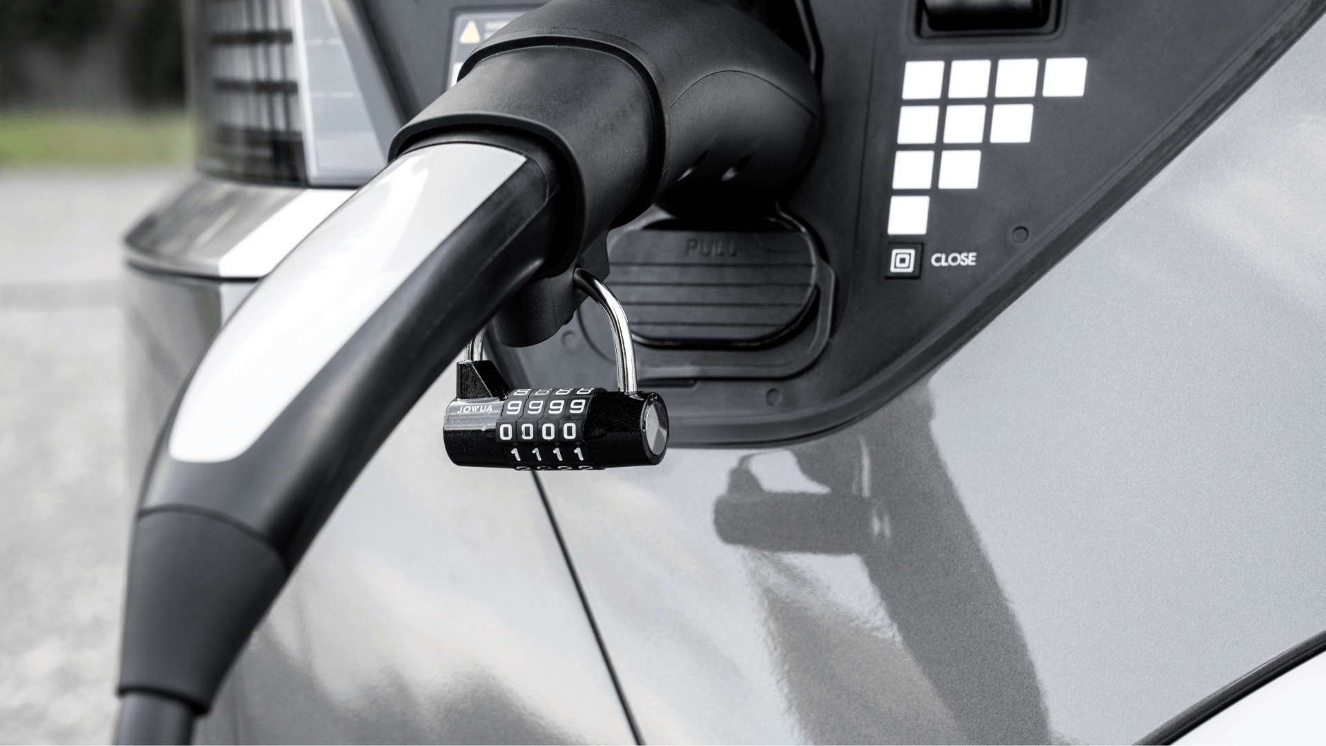 特寫展示JOWUA台灣CCS1快慢充萬用組電動車充電器連接至汽車,展示與第三方網路的兼容性。銀色密碼鎖將其固定,而汽車的外部則閃爍著金屬灰色的光芒。.