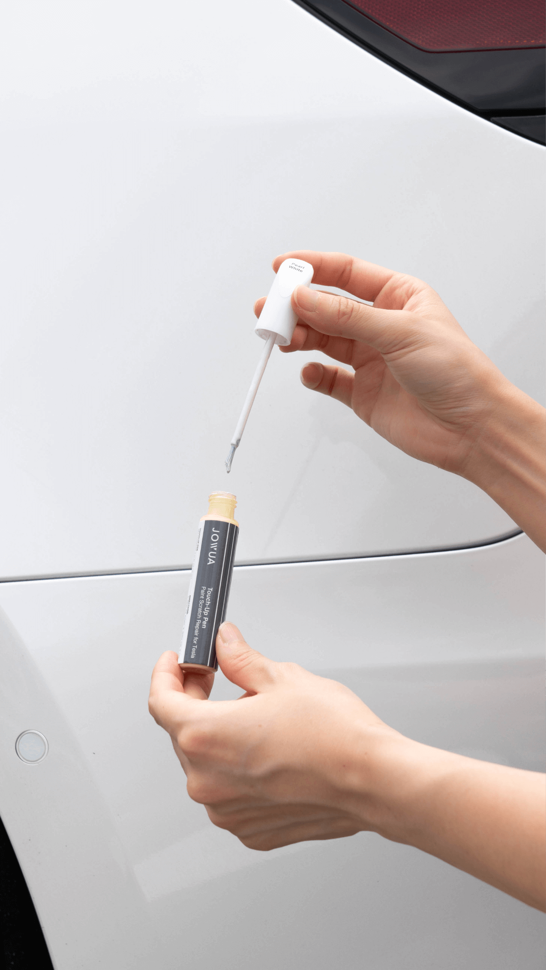 一個人熟練地用補漆筆在白色汽車附近進行快速修復,刷子塗抹器確保每個細節與特斯拉顏色無縫對齊。焦點集中在他們的手和汽車光滑表面上的油漆。台灣JOWUA產品。.