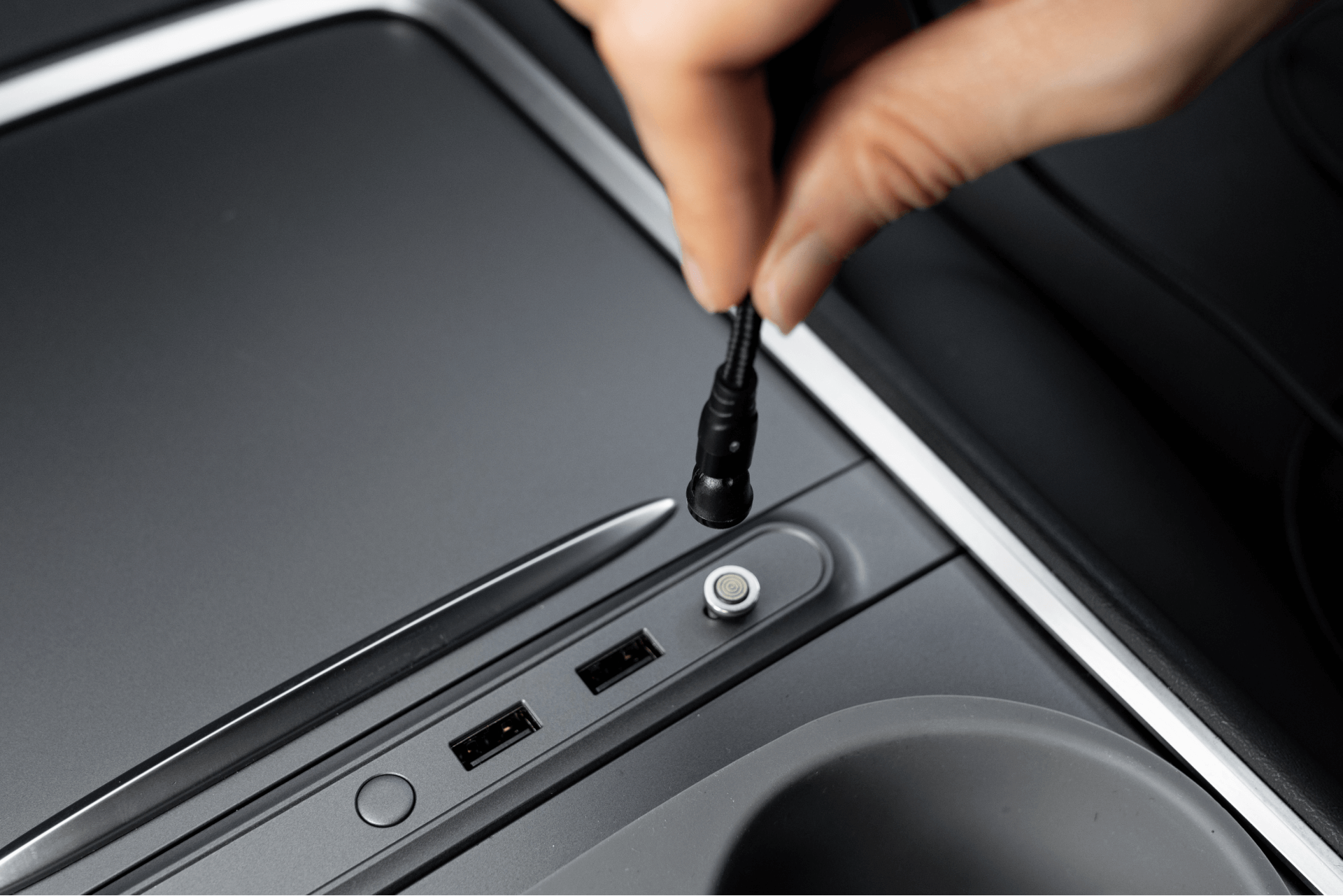 一個人使用JOWUA台灣USB-C車用磁吸線(0.4M/1M/1.8M)將線連接到車內的電子設備。這款光滑的金屬設備有兩個 USB 連接埠和一個圓形按鈕,體現了 Model 3中控的優雅設計和先進的連接性。.
