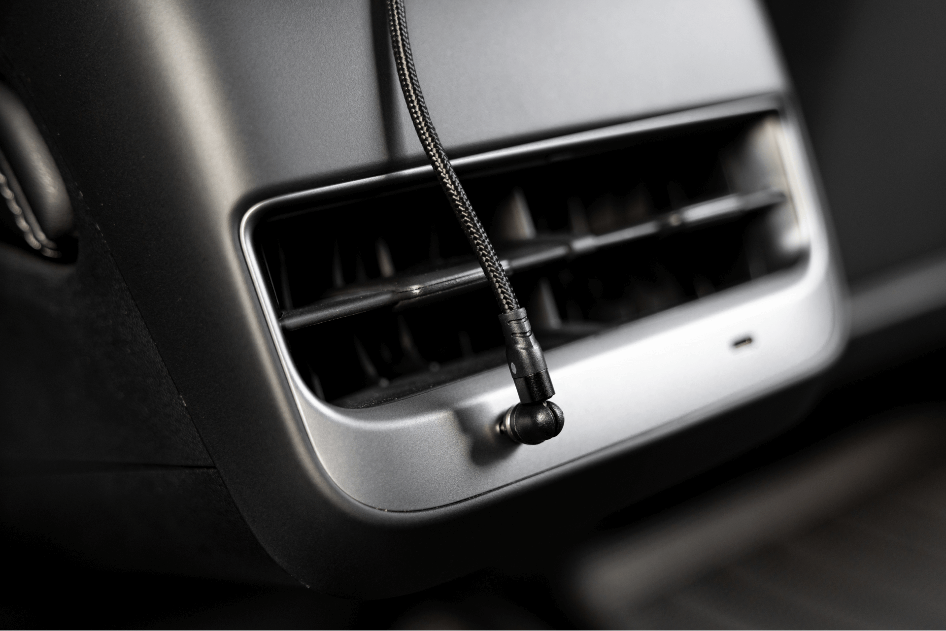 JOWUA 台灣 USB-C 車用磁吸線懸掛在汽車光滑儀表板上的後部通風口前。通風口採用帶有金屬裝飾的水平板條,凸顯了電纜的質感和現代設計,非常適合 Model 3中控的美感。.