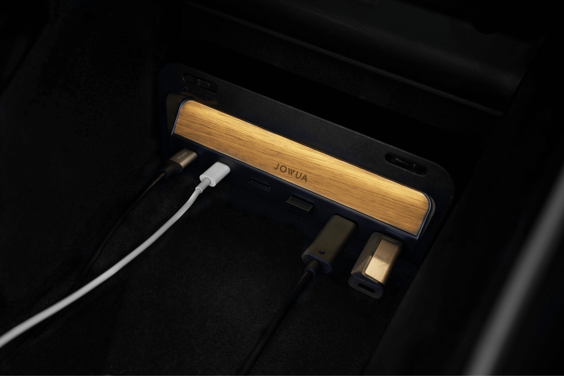 汽車內的木製 JOYJUA USB 集線器的特寫，其中多個設備透過白色、黑色和灰色的充電線連接。.