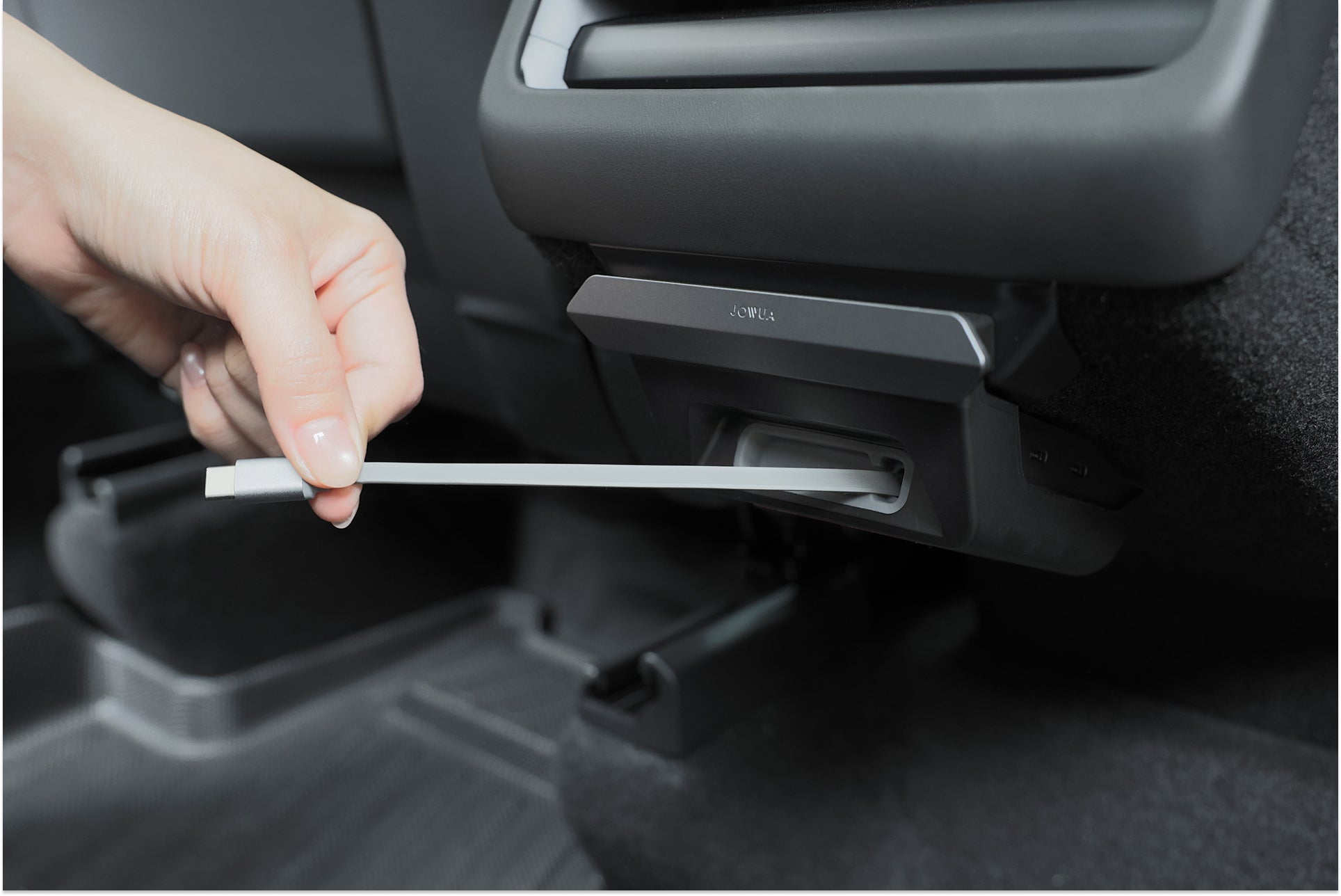 一隻手將 USB 傳輸線插入座椅後方的 130W 後排 HUB 連接埠，突顯 JOWUA Taiwan 的一幕瞭然【Model 3 煥新版｜交車禮包】為車內必備的 Model 3 配件。.