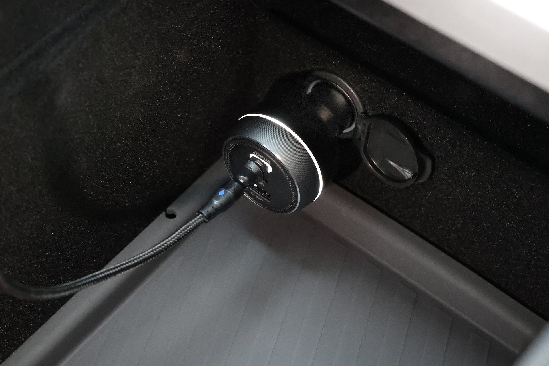JOWUA Taiwan 165W PD3.1 高效能車充的特寫，圖中 USB 線插入車內的 12V 電源插座，位於帶有紋理的橡膠地墊上方。.