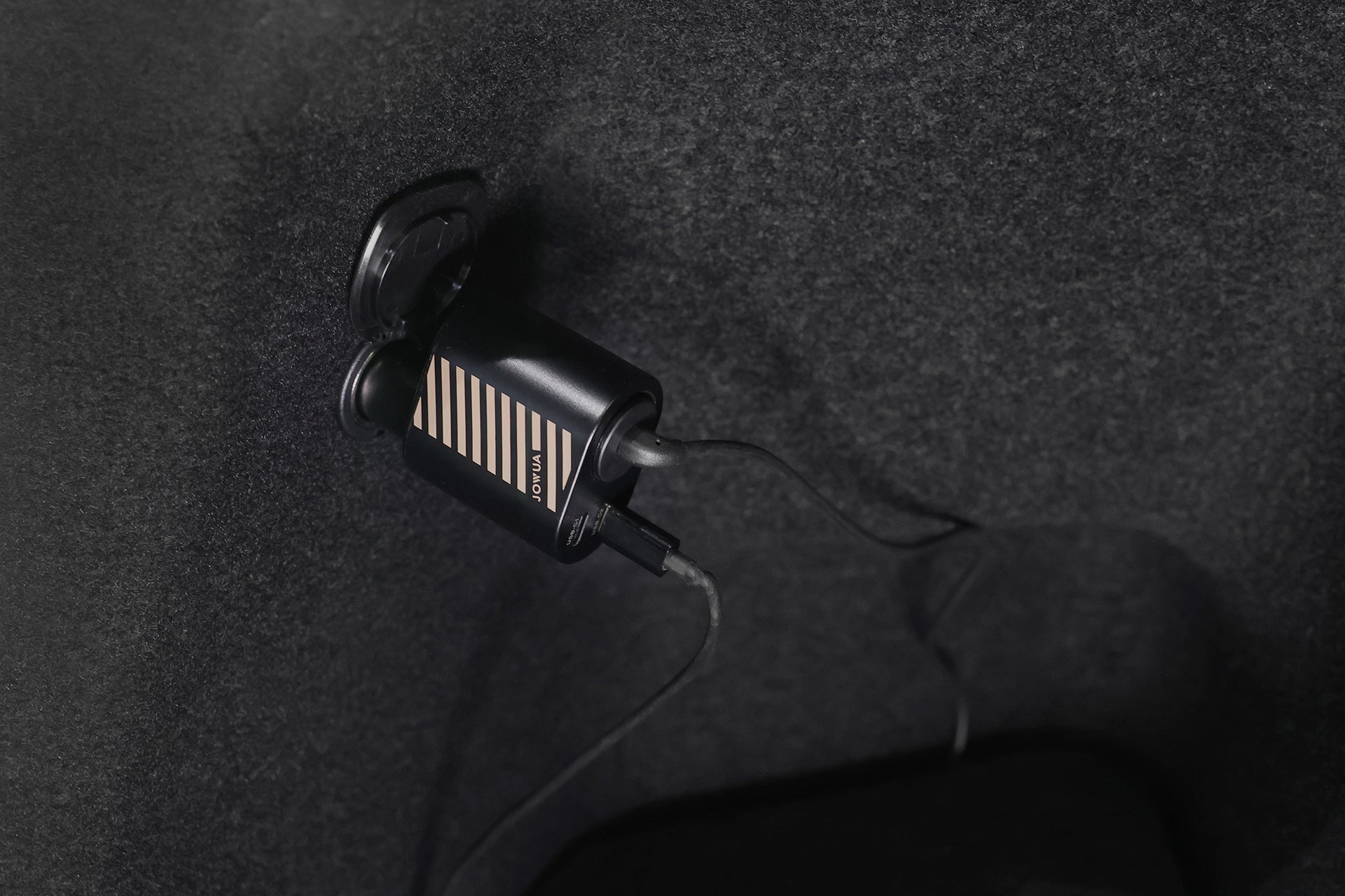 JOWUA Taiwan 三合一 Type-C 擴充點菸器充插在深色地毯上的特寫。它的連接線標榜 200W 大功率和 Type-C點菸器轉接頭，滿足多樣化的充電需求。.