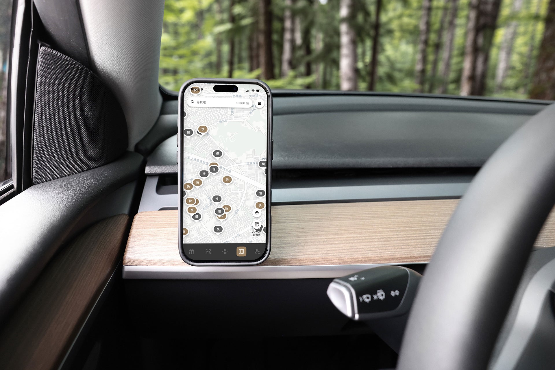 JOWUA Taiwan Qi2 製冷出風口 MagSafe 車架 (Model 3/Y 2018-2024)上安裝了一部地圖智慧型手機，附在車子的出風口。木質鑲板、部分方向盤，以及車外的森林都清晰可見。.