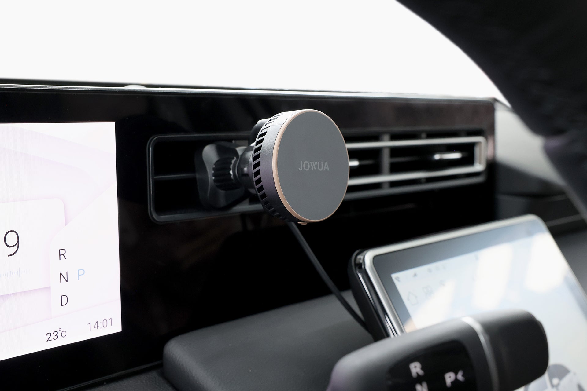 汽車儀表板的特寫，顯示 JOWUA Taiwan Qi2 製冷出風口車架 (MagSafe 款) 電話固定座透過連接線固定在出風口上。數位顯示器和排檔也清晰可見。.