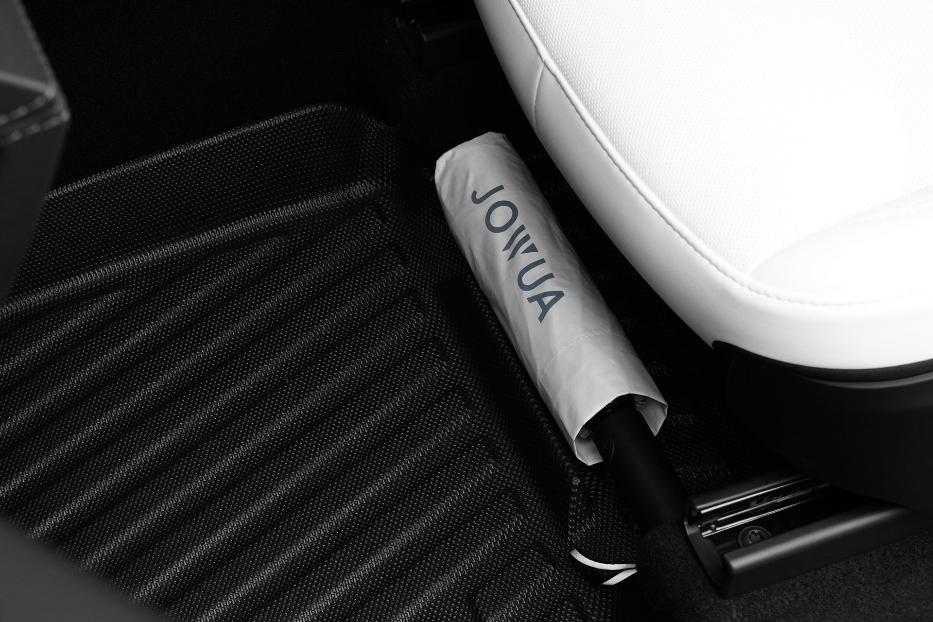 白色座椅旁的JOWUA台灣立體防水墊+面紙盒組合（Model Y 2021-2025+）上放置著一把帶有JOYUA標誌的折疊白色雨傘，展示了特斯拉Model Y的智慧收納設計。.