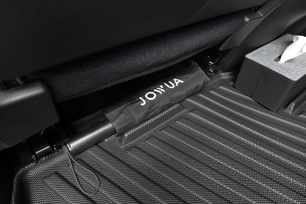 一件黑色、標有「JOWUA 台灣」品牌的物品（可能是把雨傘），被放置在 Foxtron Cavira 立體防水腳踏墊上的一張汽車座椅下方；這款腳踏墊以「全面防護車用腳踏墊」的設計而聞名。 一旁放著一盒面紙，而腳踏墊的紋理表面則能增強抓地力，並為放置在座椅下方的物品提供額外保護。.