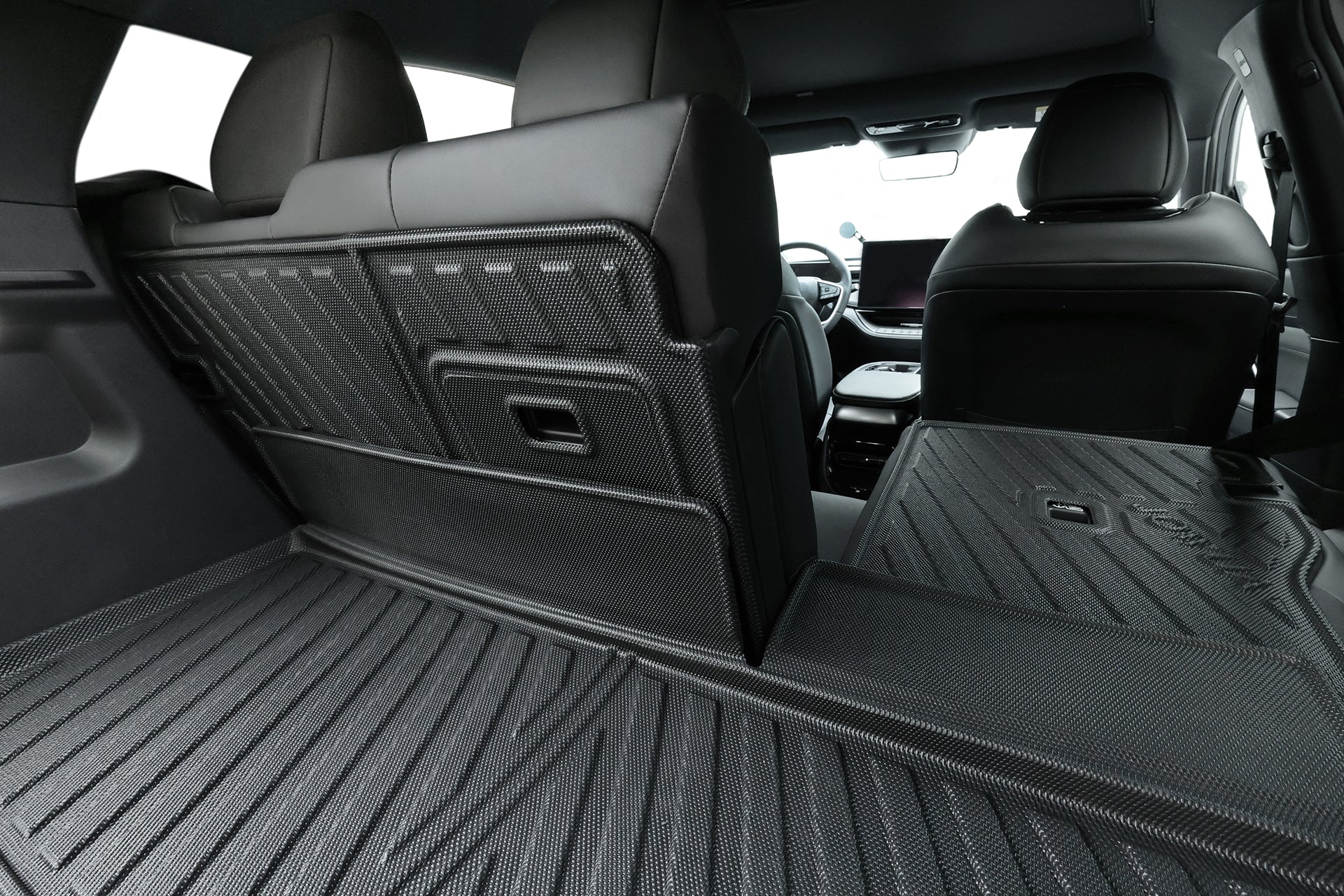 從一張座椅直立和一張座椅摺疊的後方貨運區觀看，寬敞的行李箱襯裡採用 JOWUA Taiwan 立體防水行李廂墊＋椅背墊組合 (Foxtron Bria)，提供耐用、防水的保護，以及時尚的黑色內裝。.